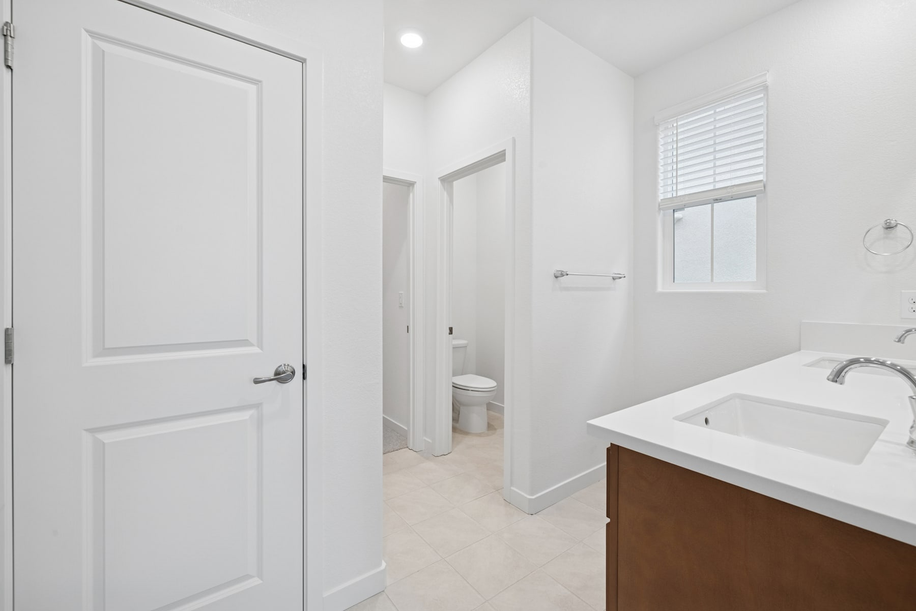 A bright and spacious bathroom with a white door, a vanity with a sink, and a window providing natural light.