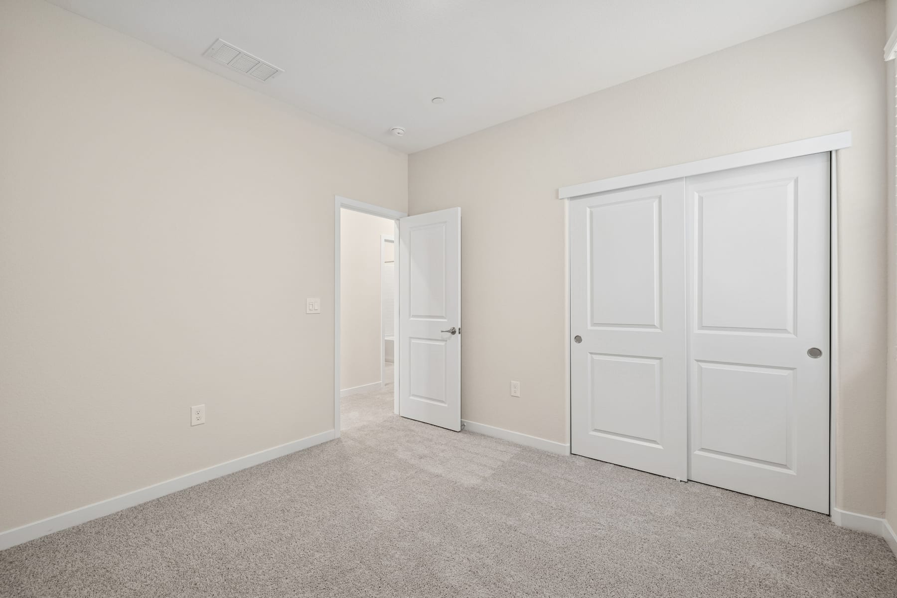 A spacious, well-lit room with white walls, a carpeted floor, and two closed doors, one of which appears to be a closet.