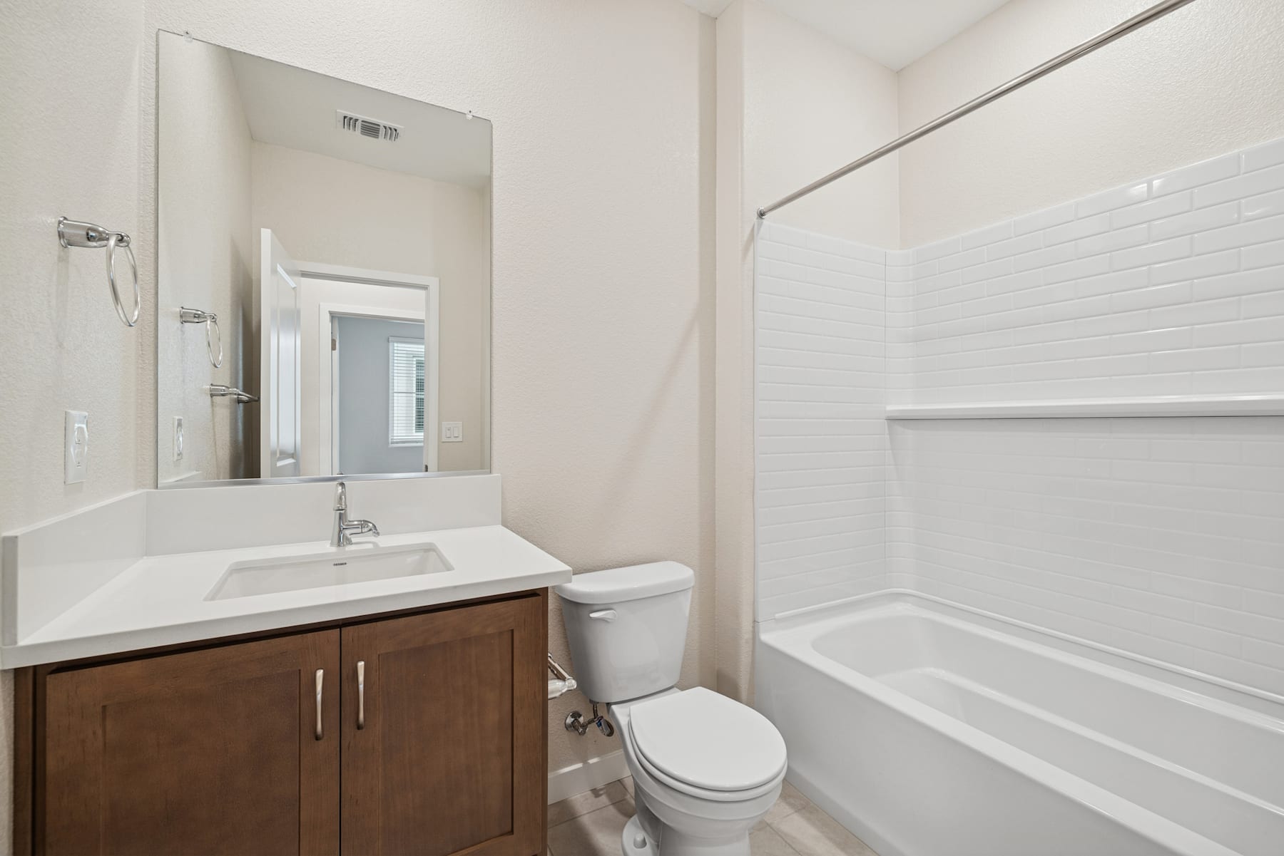 A modern, minimalist bathroom with a wooden vanity, a white sink, and a bathtub surrounded by white walls and a window.