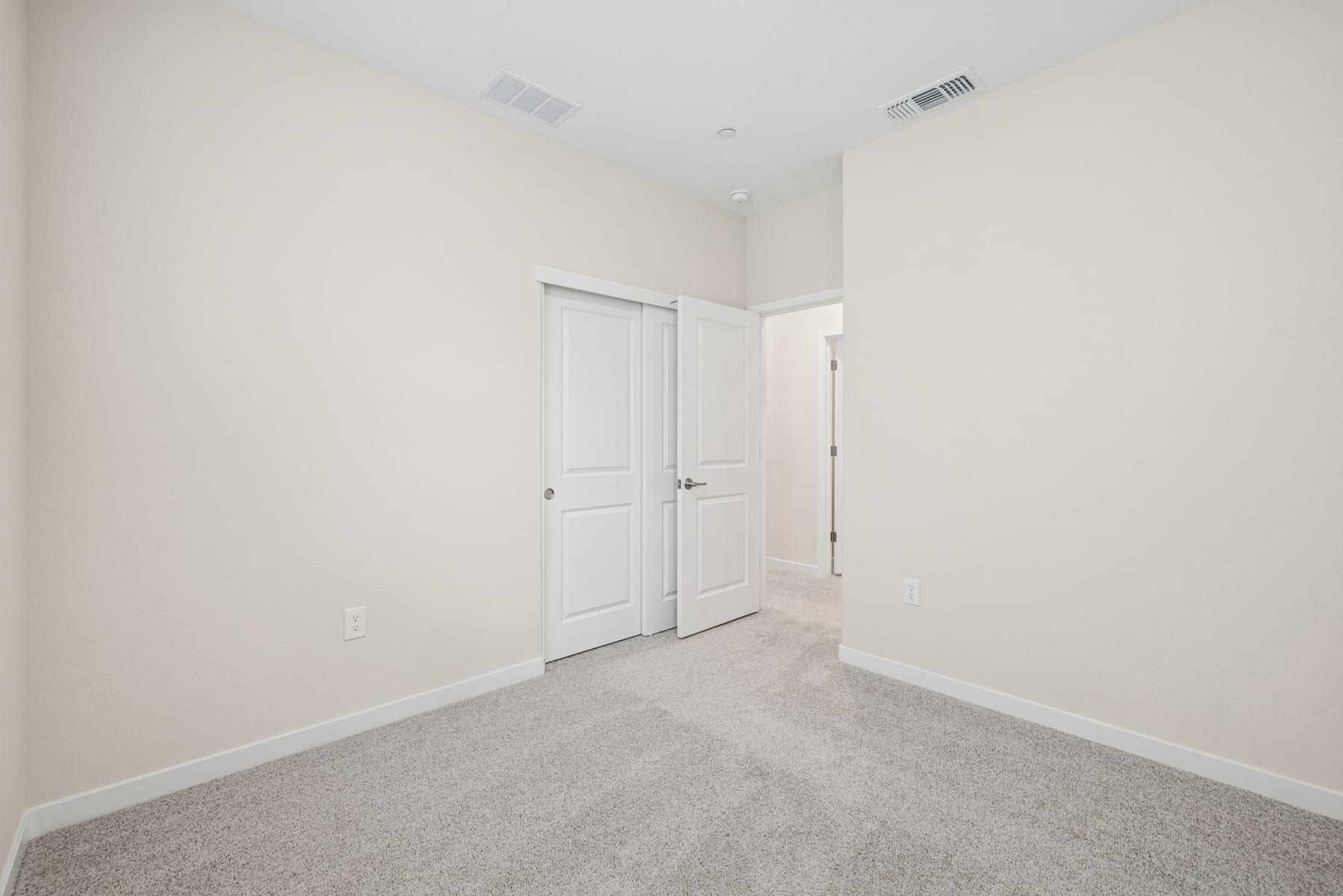A simple, minimalist room with white walls, a closed door, and gray carpeting covering the floor.