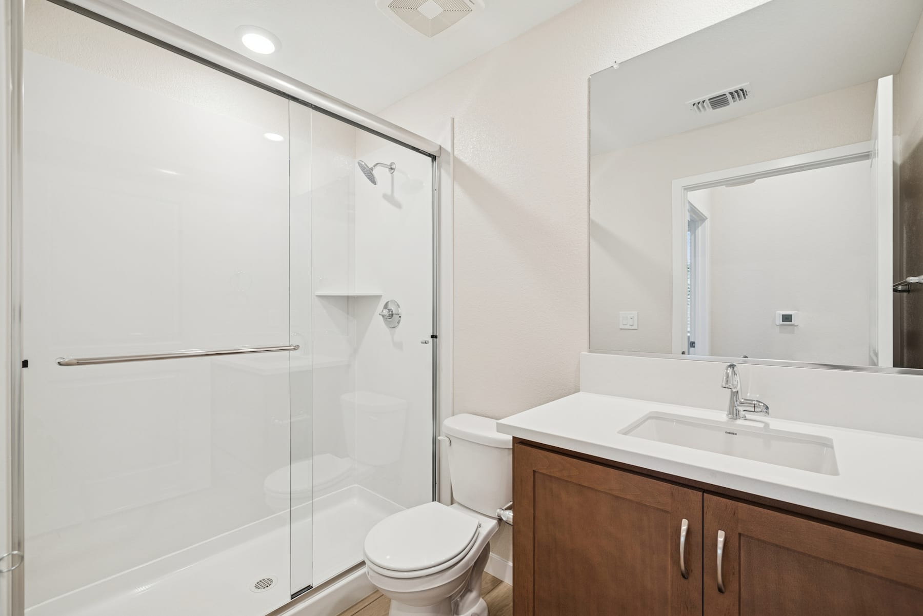 A modern, minimalist bathroom with a white vanity, a large mirror, and a glass shower enclosure.