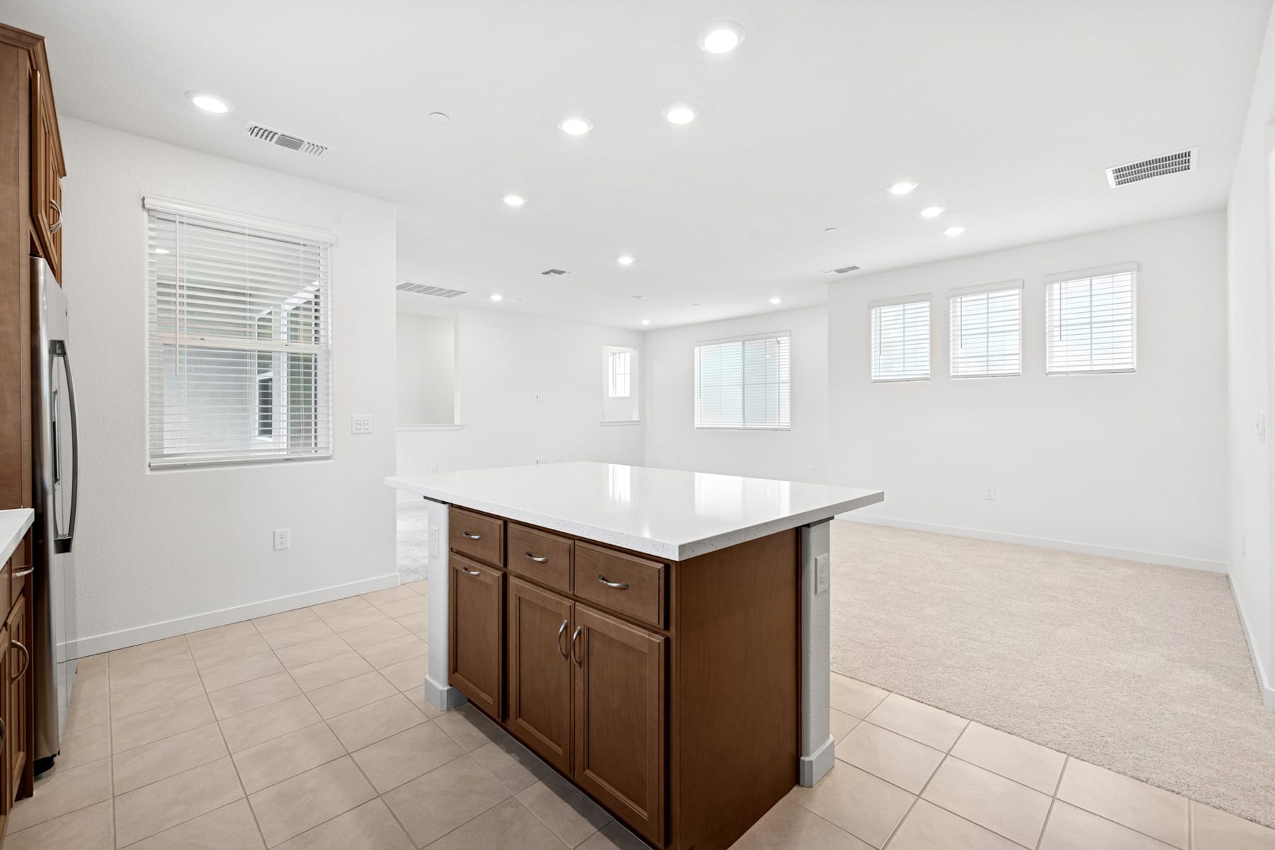 A spacious, well-lit room with a kitchen island and wooden cabinets, surrounded by large windows and a tiled floor.