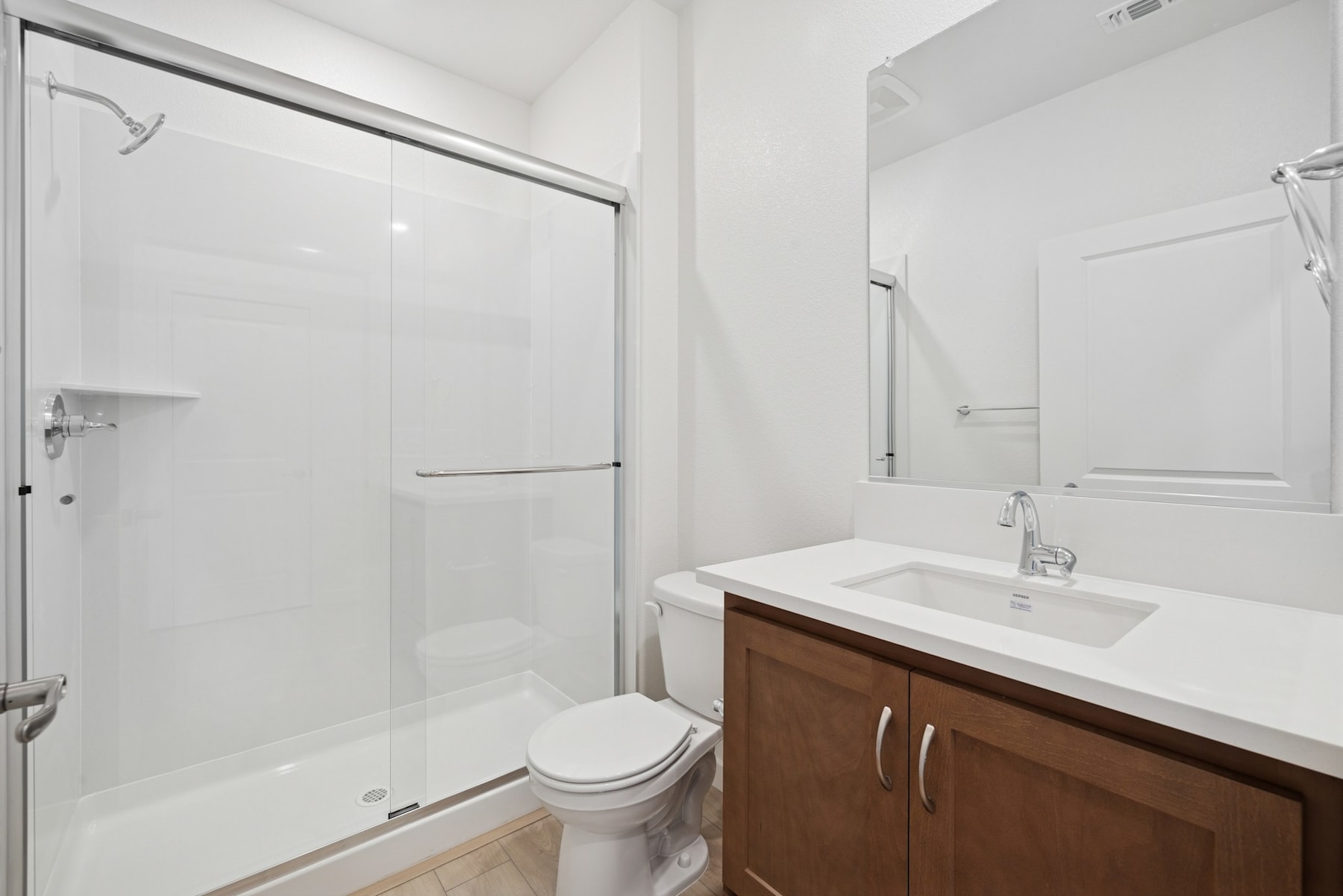 A modern, minimalist bathroom with a white vanity, a large mirror, and a glass-enclosed shower.