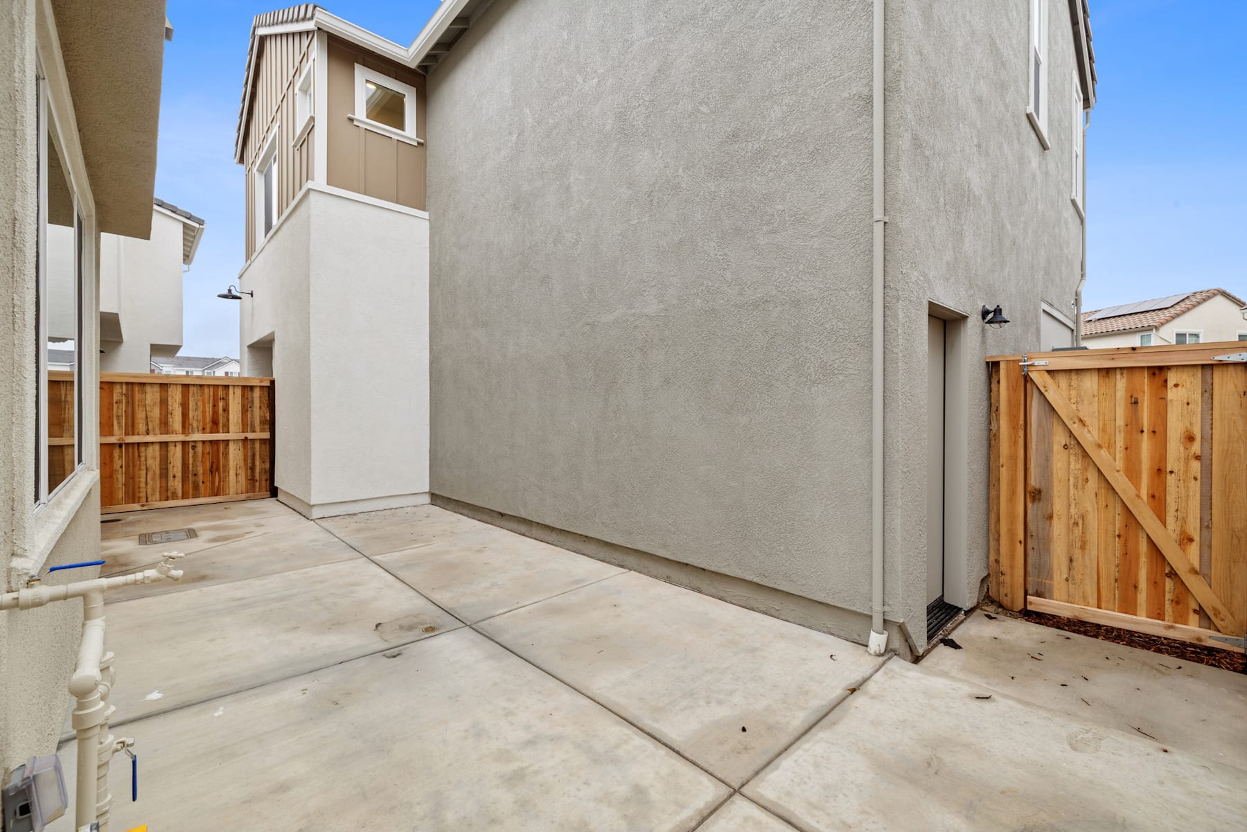 A concrete walkway leads to a wooden gate, with a tall, beige-colored building visible in the background.