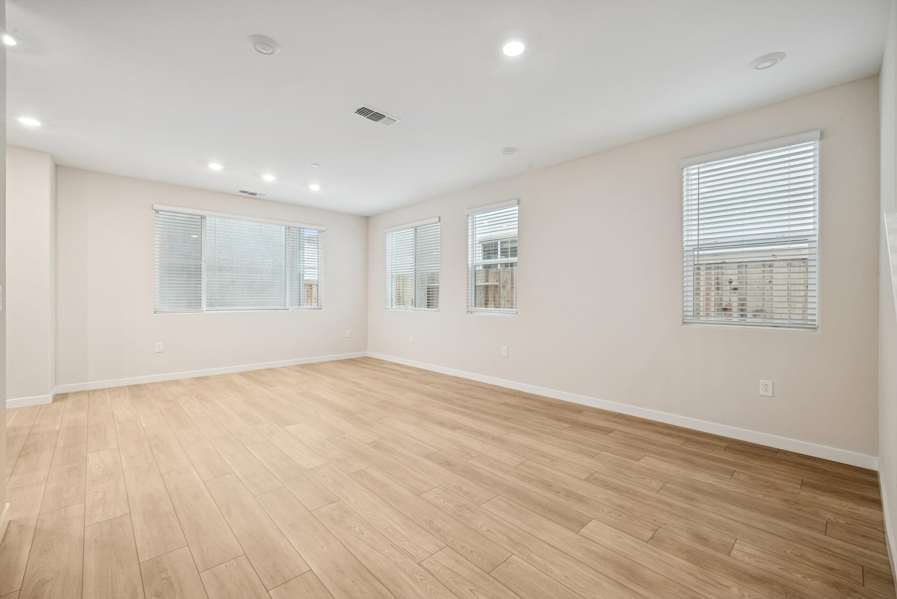 An empty, well-lit room with hardwood floors, white walls, and several windows providing natural light.
