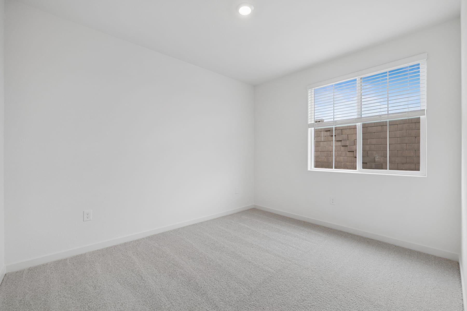 A bright, empty room with a large window and white walls, featuring a plain gray floor.