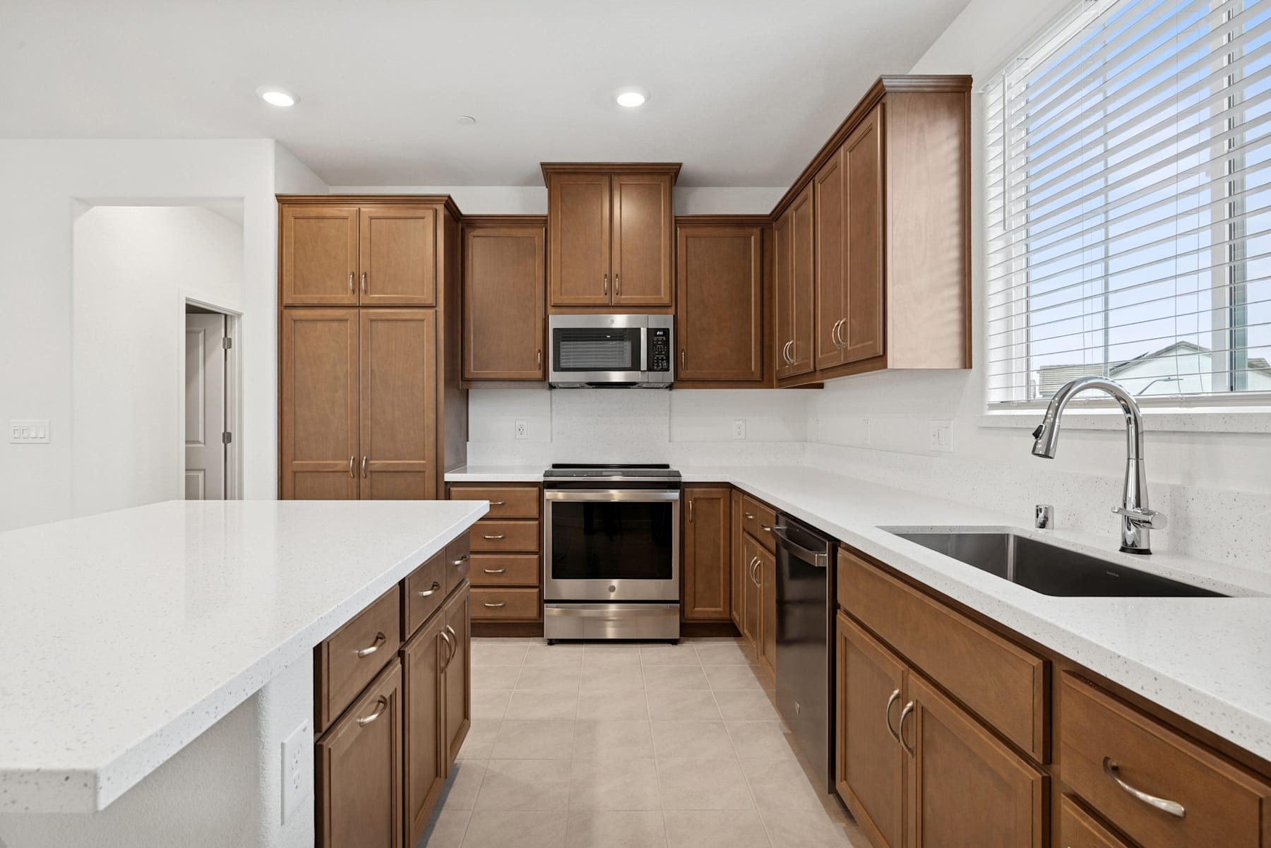 A modern, well-equipped kitchen with wooden cabinets, stainless steel appliances, and a white countertop that extends along the length of the room.
