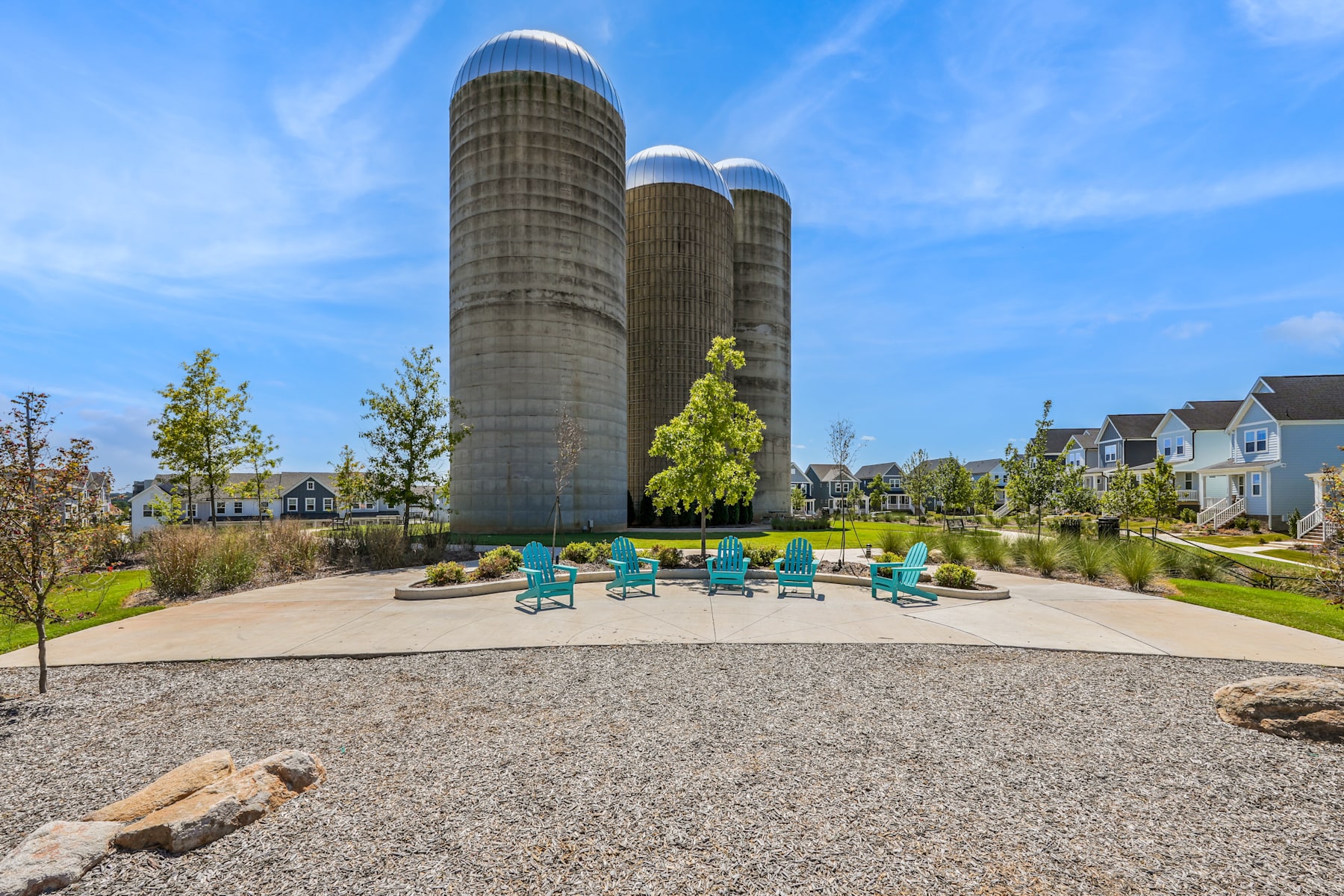 The image depicts a scenic outdoor area with three large silos in the background, surrounded by a grassy landscape with colorful Adirondack chairs in the foreground.