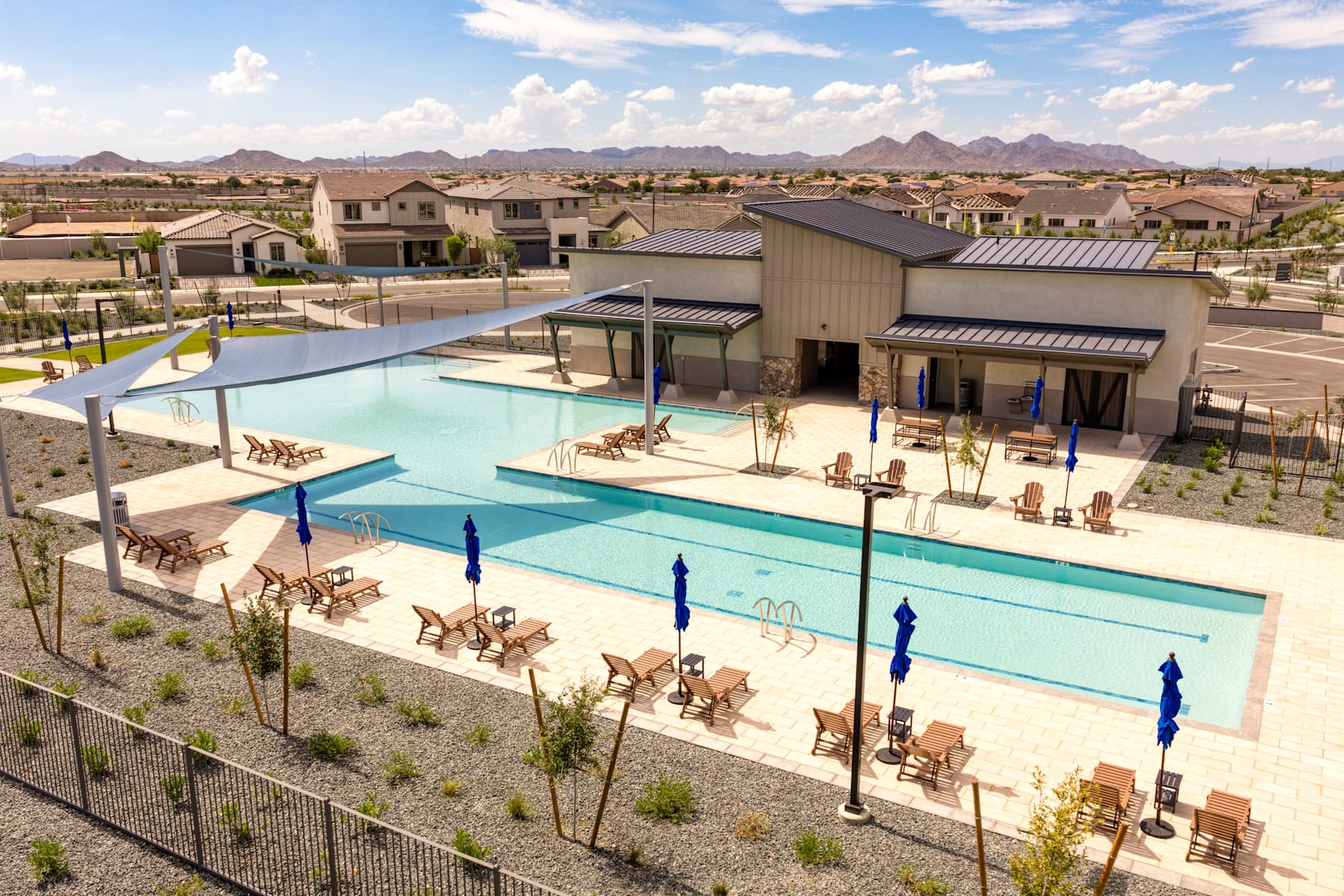A residential community with a large swimming pool surrounded by buildings, chairs, and a mountainous landscape in the background.