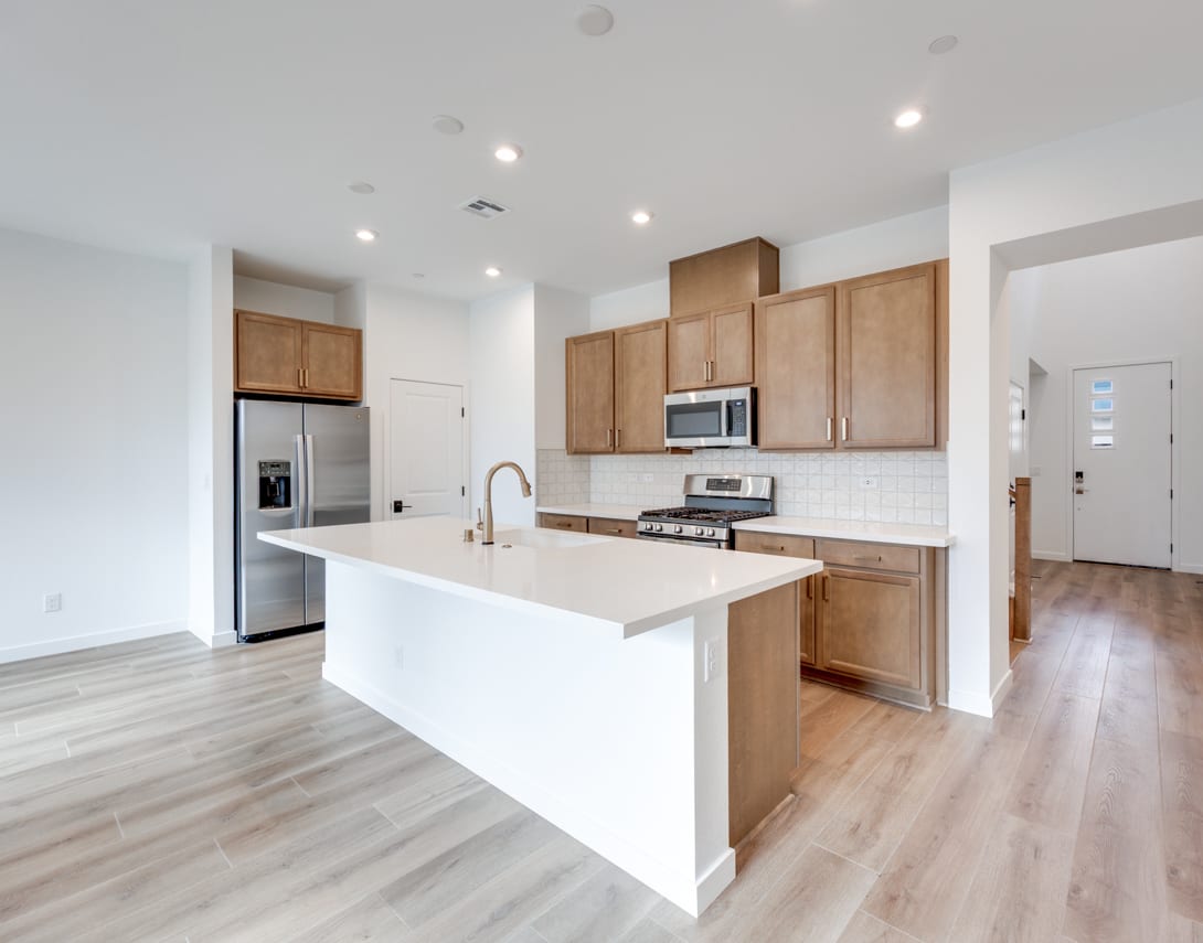 A modern, open-concept kitchen with light wood cabinets, a white countertop, and stainless steel appliances, set against a backdrop of hardwood floors and a bright, airy space.