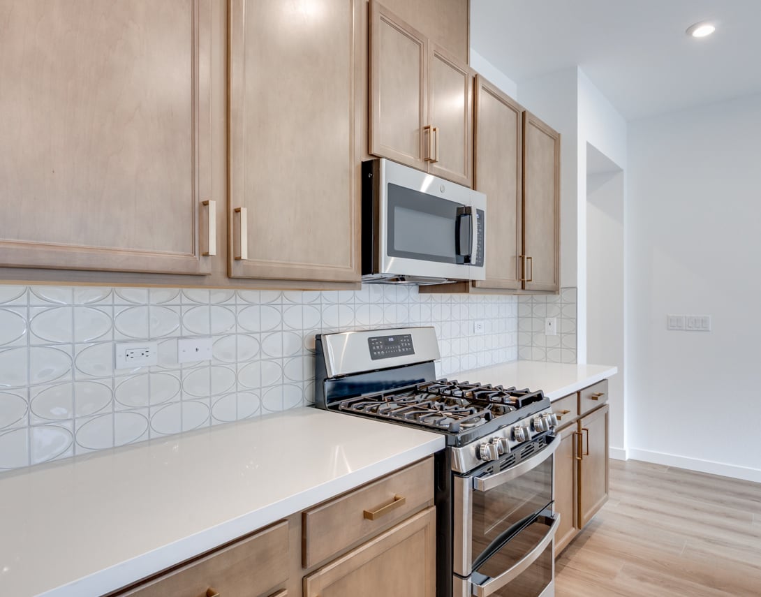 A modern kitchen with light-colored cabinets, a gas stove, and a microwave oven built into the wall, set against a tiled backsplash.