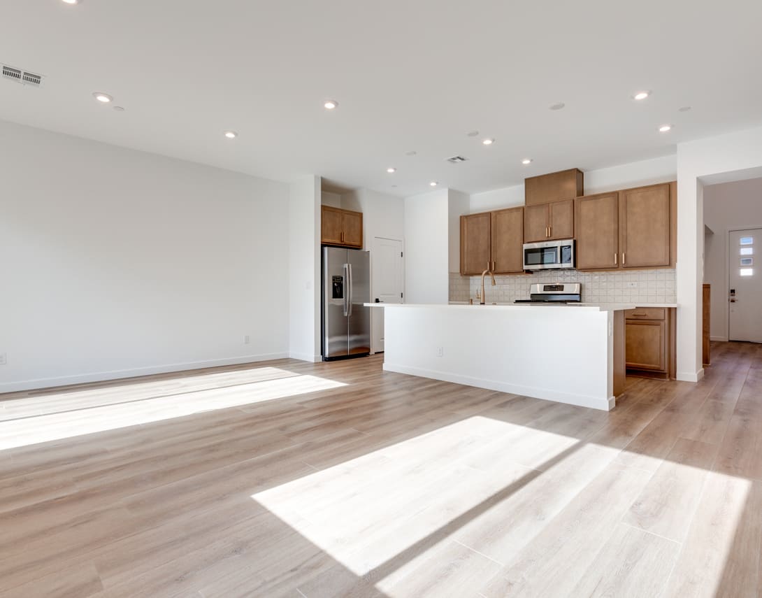 A spacious and bright open-concept kitchen and living room with wooden cabinets, stainless steel appliances, and hardwood flooring.