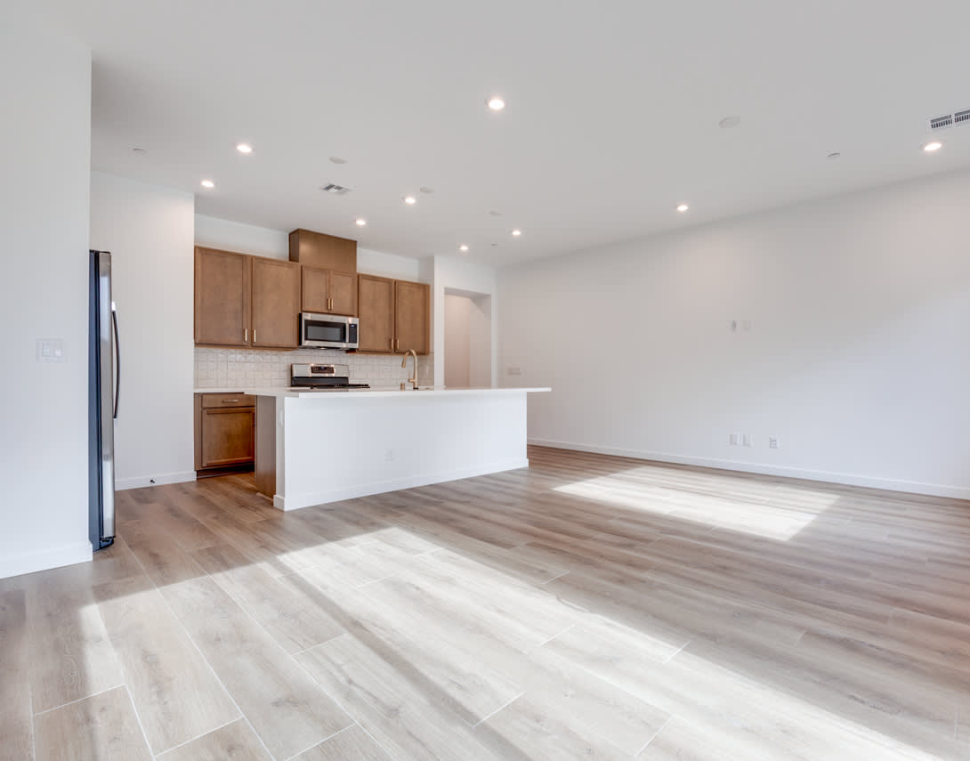 A spacious, open-concept living area with a kitchen featuring wooden cabinets and a white countertop, along with a hardwood floor that extends throughout the room.
