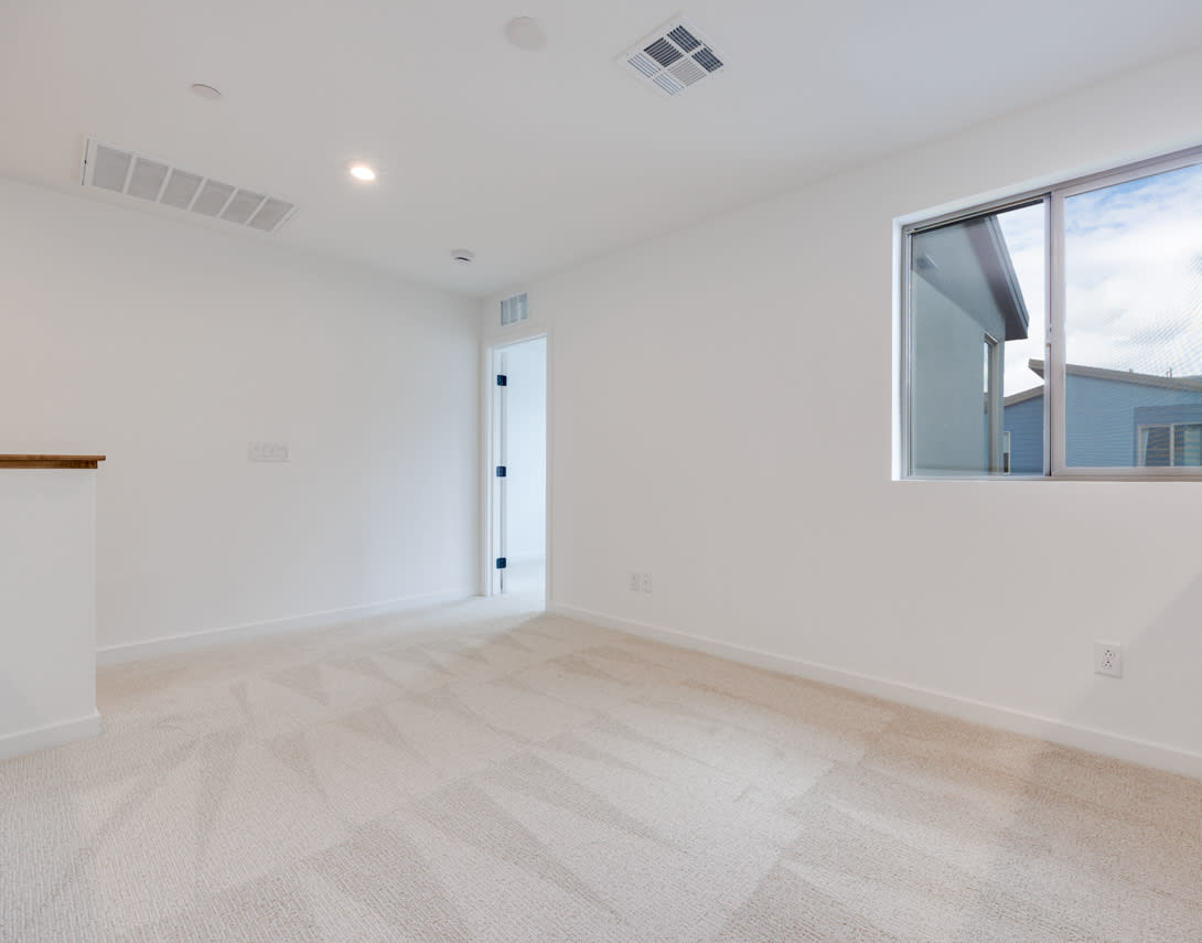 A bright, spacious room with a large window, hardwood floors, and a white door.