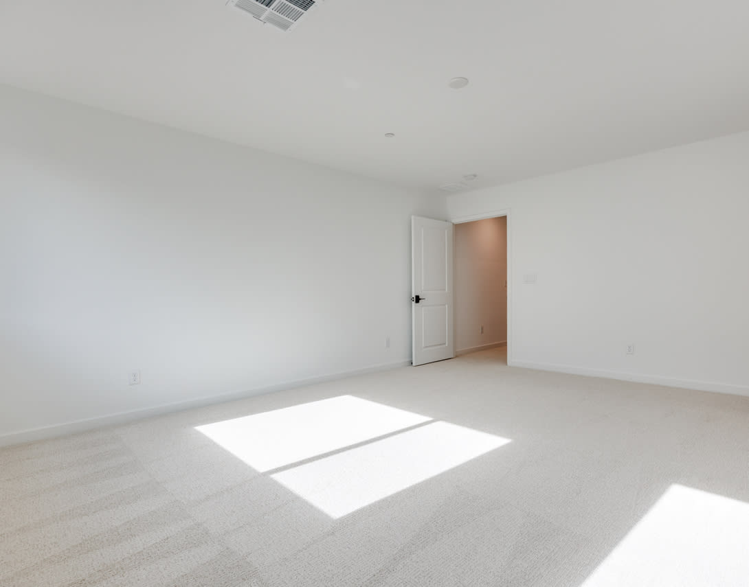 A bright, empty room with a white wall, a closed door, and a patch of sunlight on the floor.