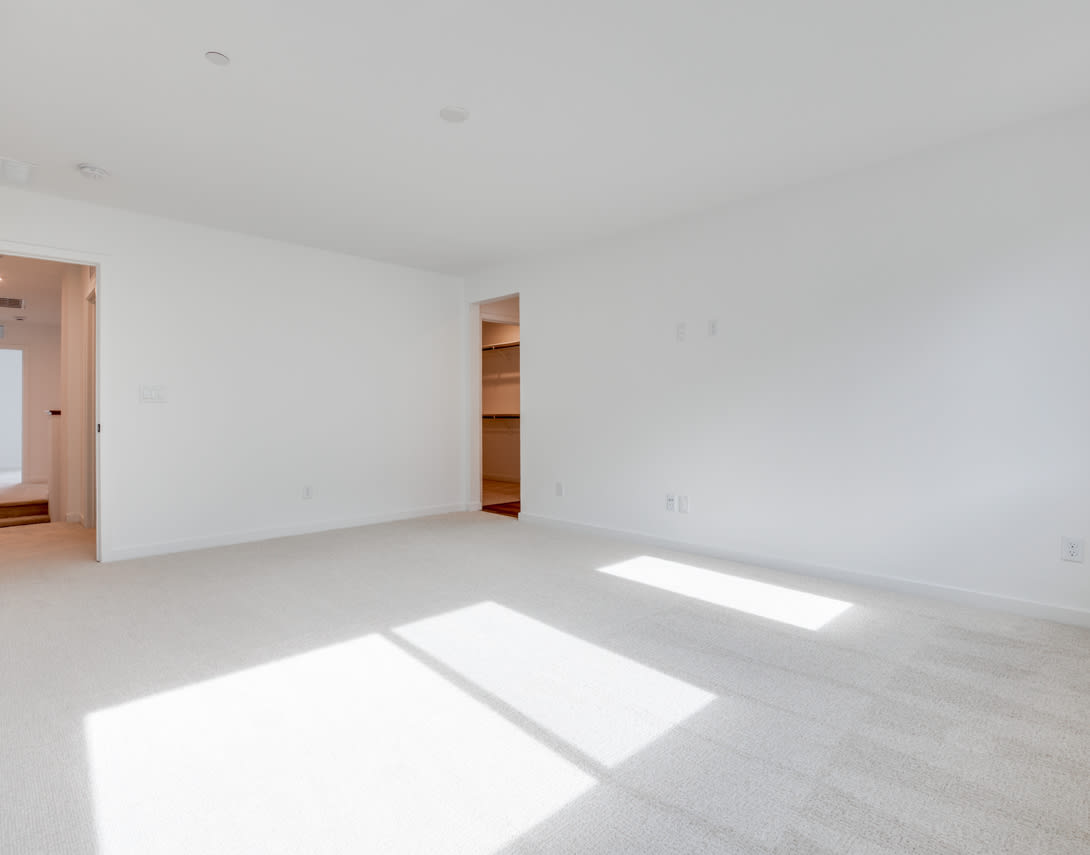 A bright, spacious room with white walls, a hardwood floor, and a closet visible in the background.