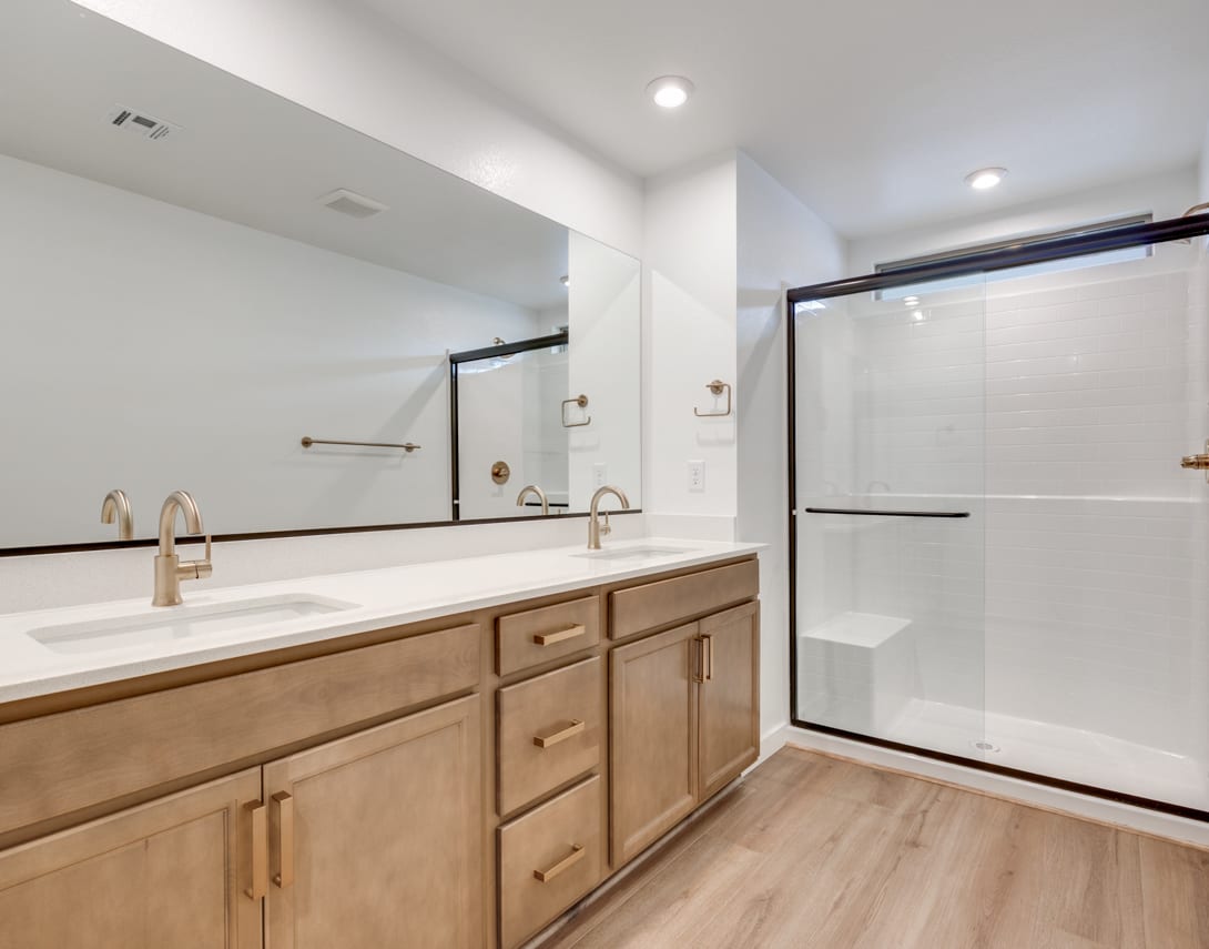 A modern bathroom with a wooden vanity, a large mirror, and a glass shower enclosure, set against a bright and airy backdrop.