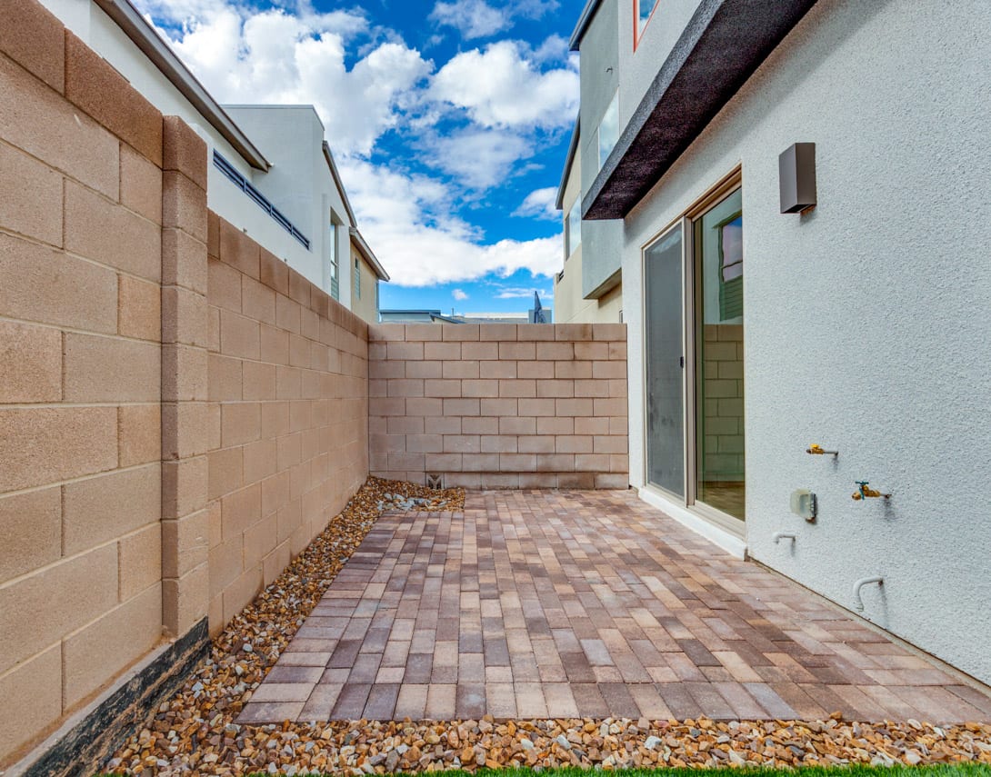 A paved walkway leads through a courtyard surrounded by beige walls, with a blue sky and fluffy clouds visible overhead.