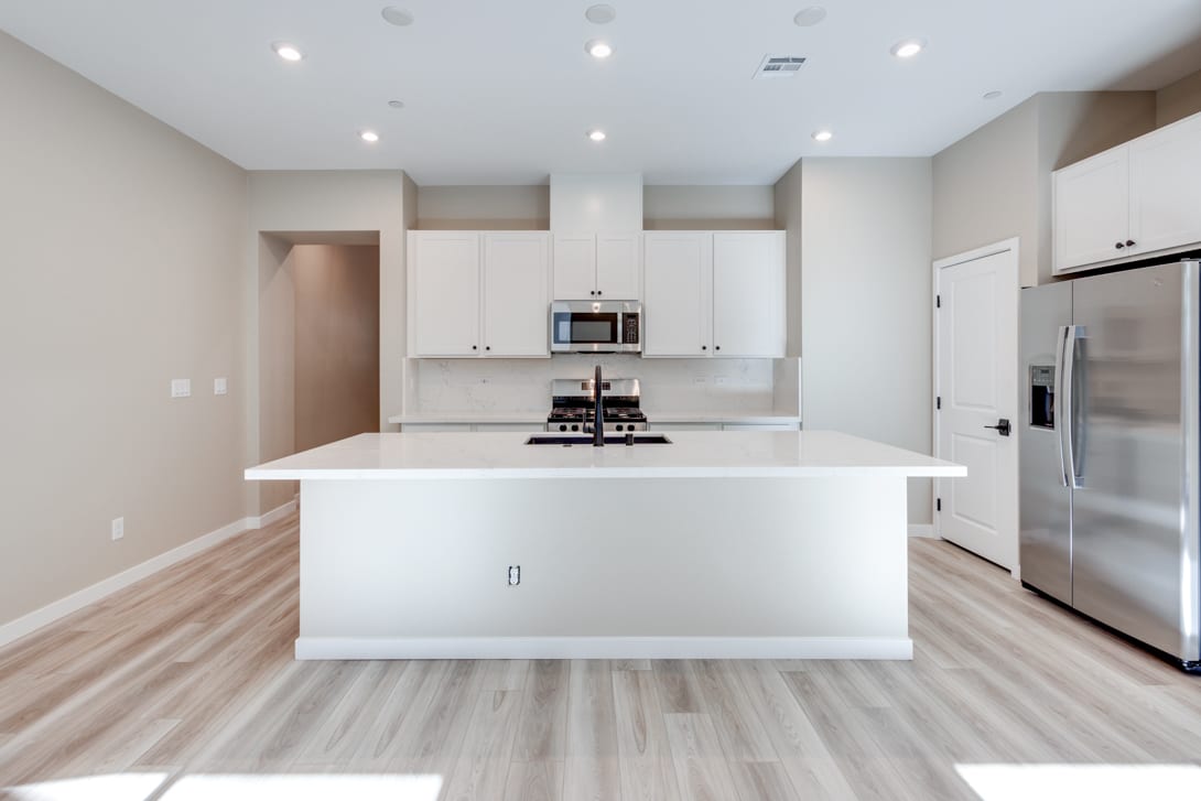 A modern, open-concept kitchen with white cabinets, a large island, and hardwood flooring, creating a bright and spacious atmosphere.