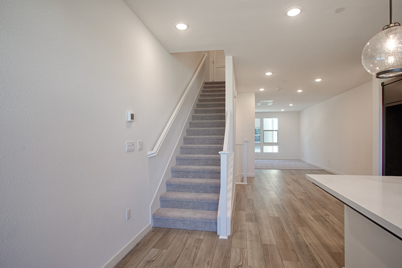 A bright and spacious interior with a wooden staircase leading up to the second floor, surrounded by white walls and a hardwood floor.