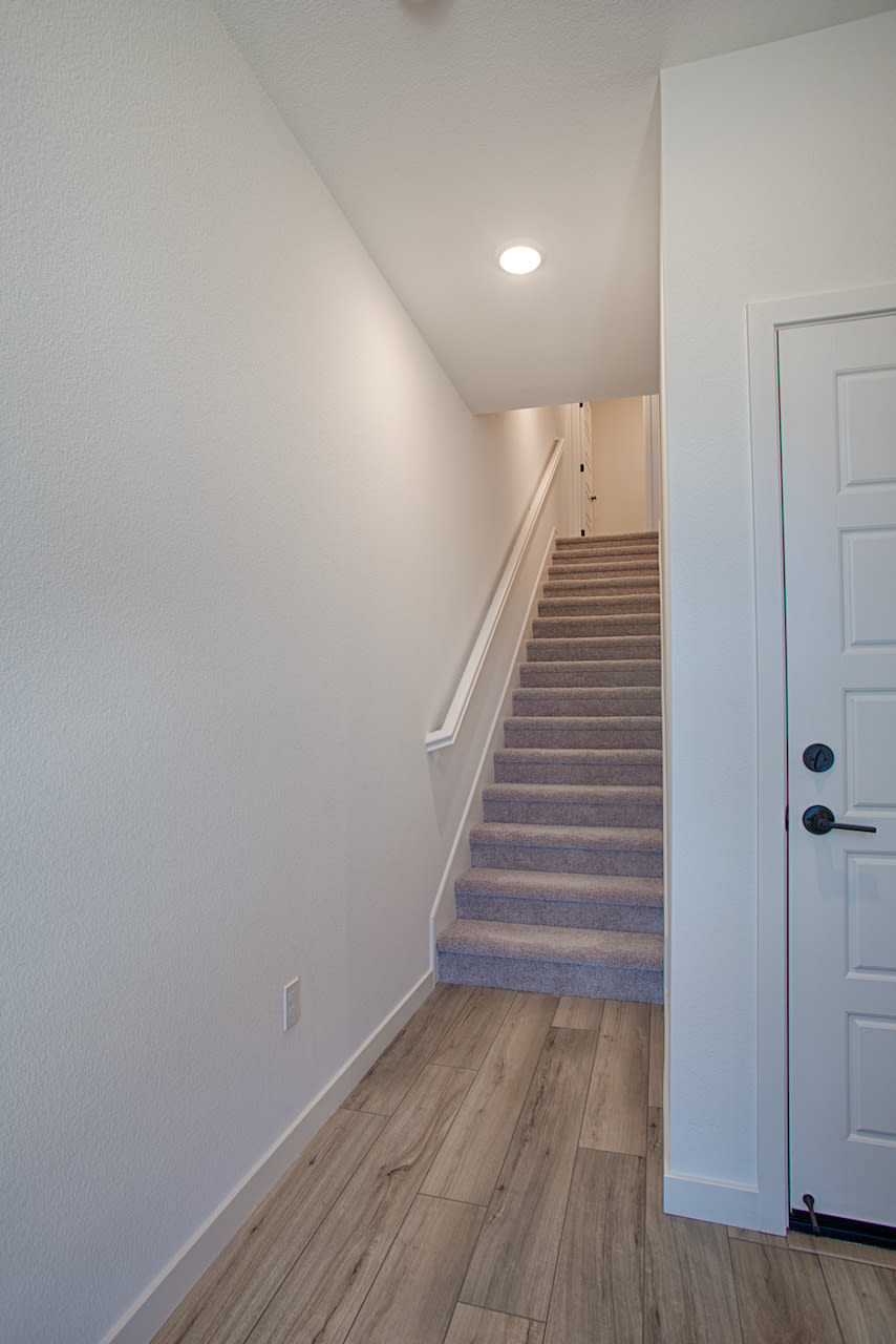 A staircase leading up to a second floor, with a white wall and a wooden floor visible in the foreground.