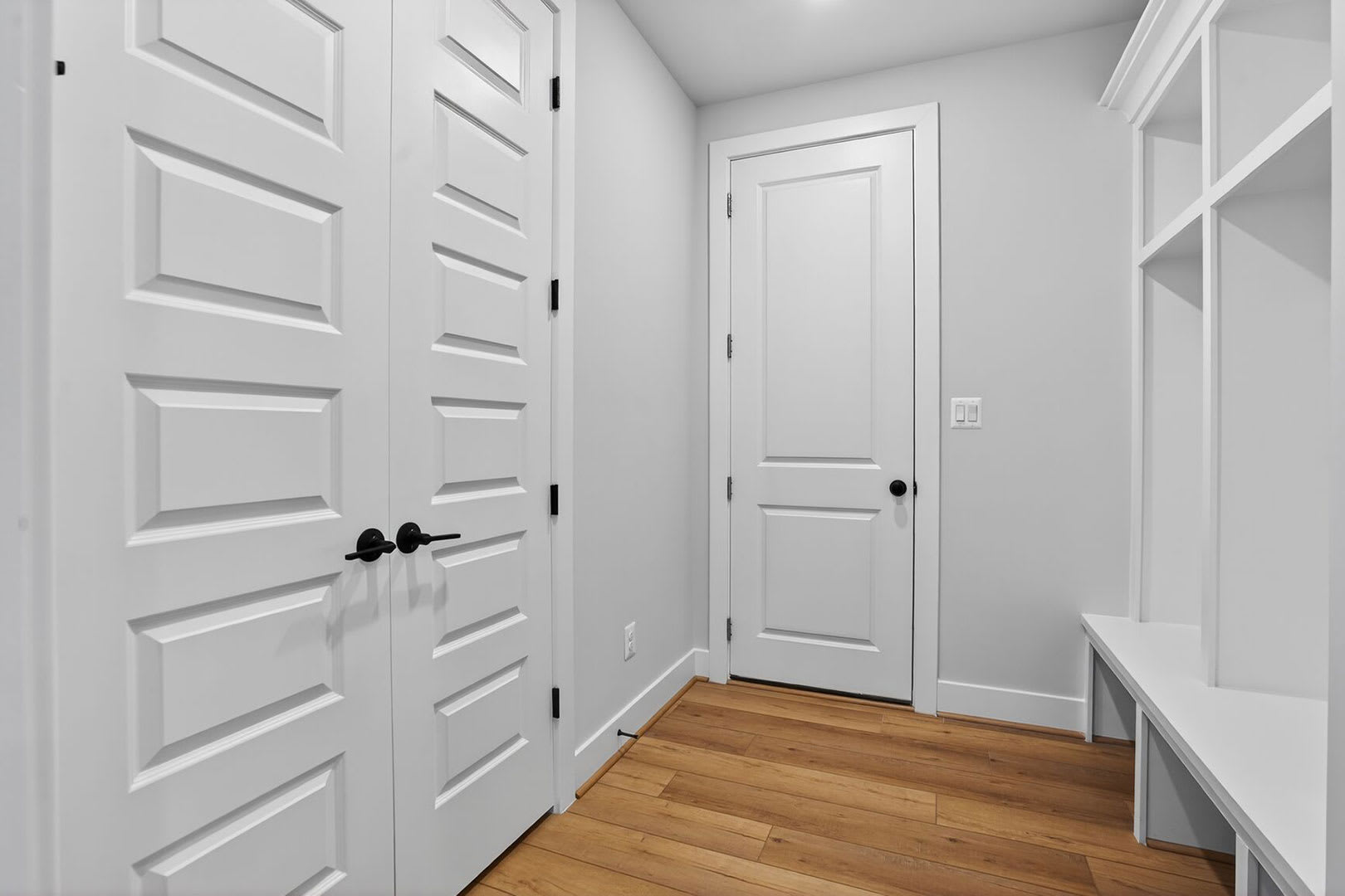 A bright, minimalist hallway with white walls, wooden floors, and a closed door leading to another room.
