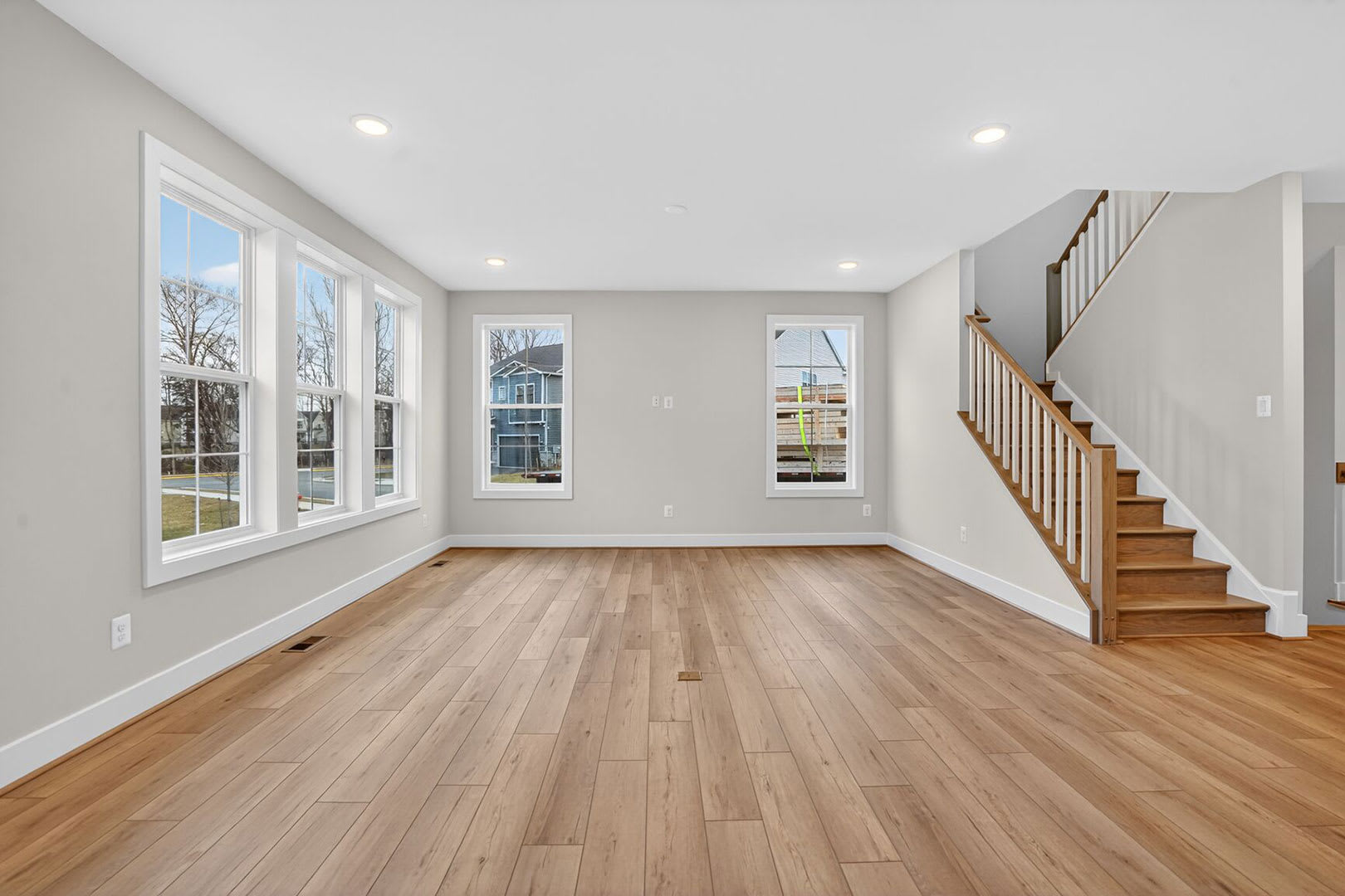 A spacious and bright living room with hardwood floors, large windows, and a staircase leading to the upper level.