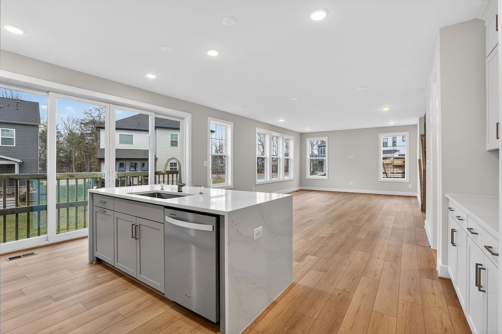 A modern, open-concept kitchen with a central island, hardwood floors, and large windows overlooking a residential neighborhood.