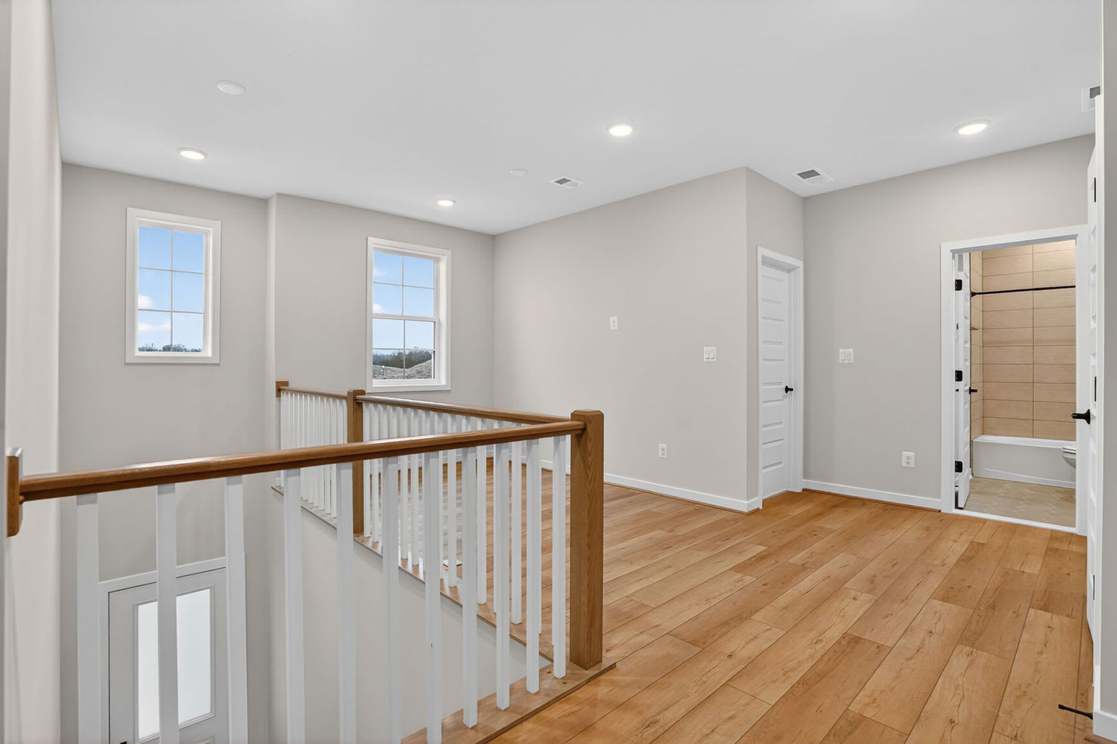 A spacious and well-lit hallway with wooden floors, a railing, and several doors leading to other rooms.