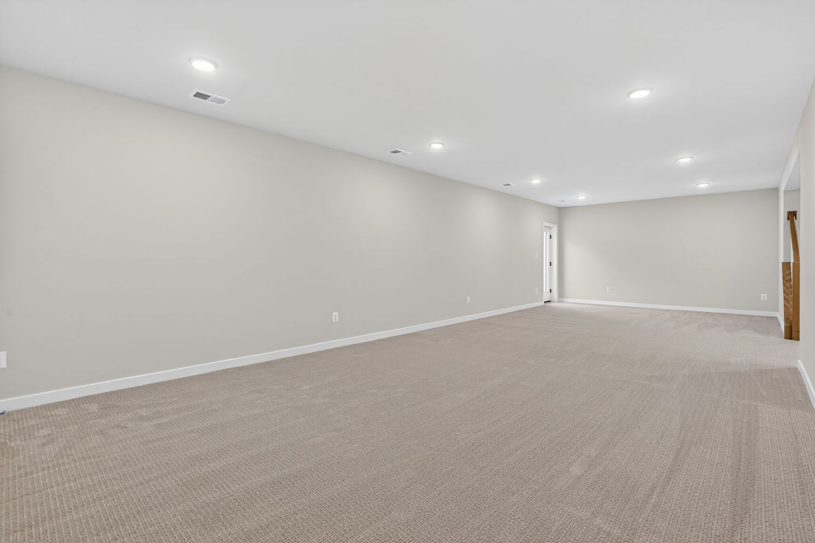 An empty room with white walls, a carpeted floor, and recessed lighting fixtures in the ceiling.