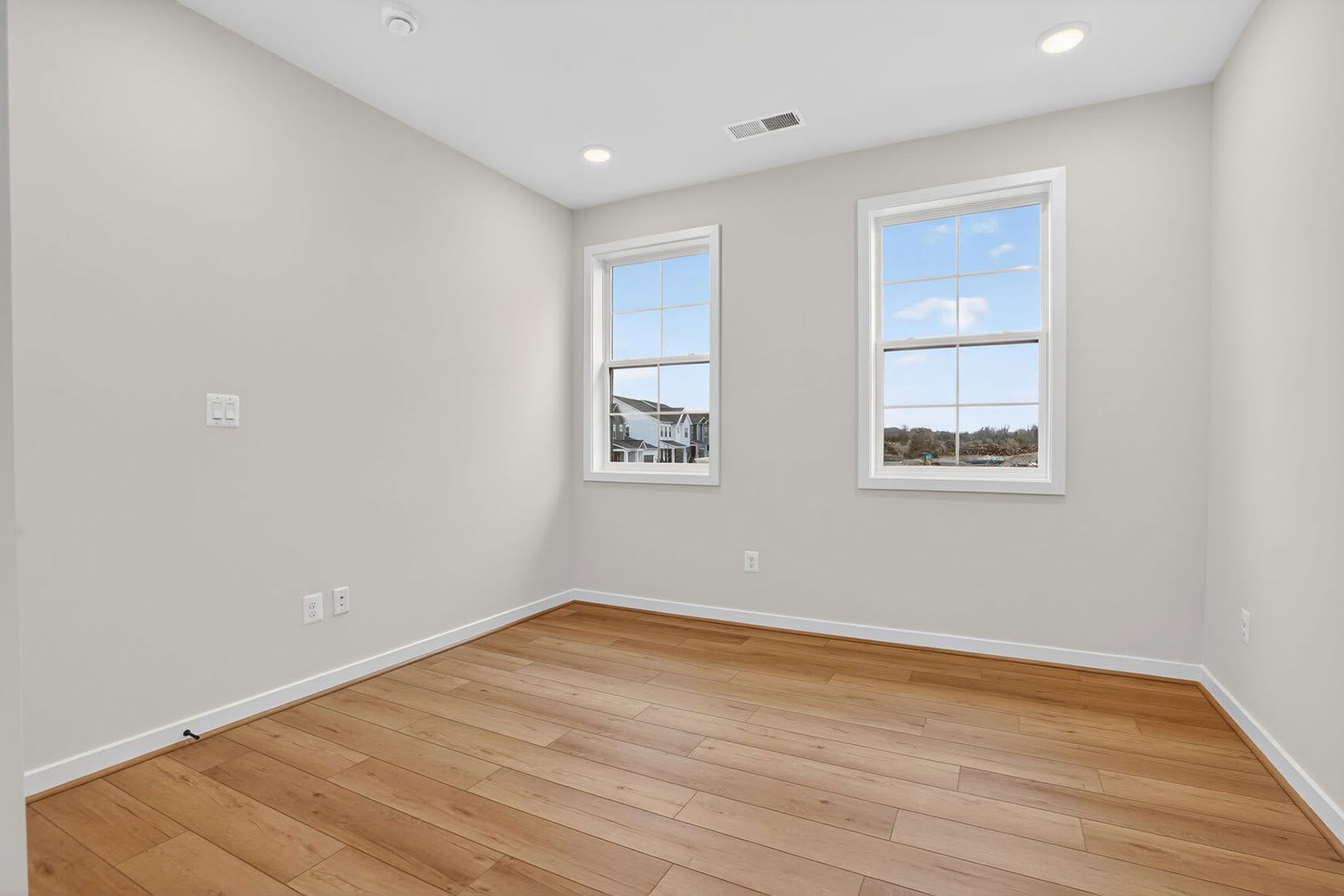 A spacious, well-lit room with hardwood floors and large windows overlooking an outdoor scene.