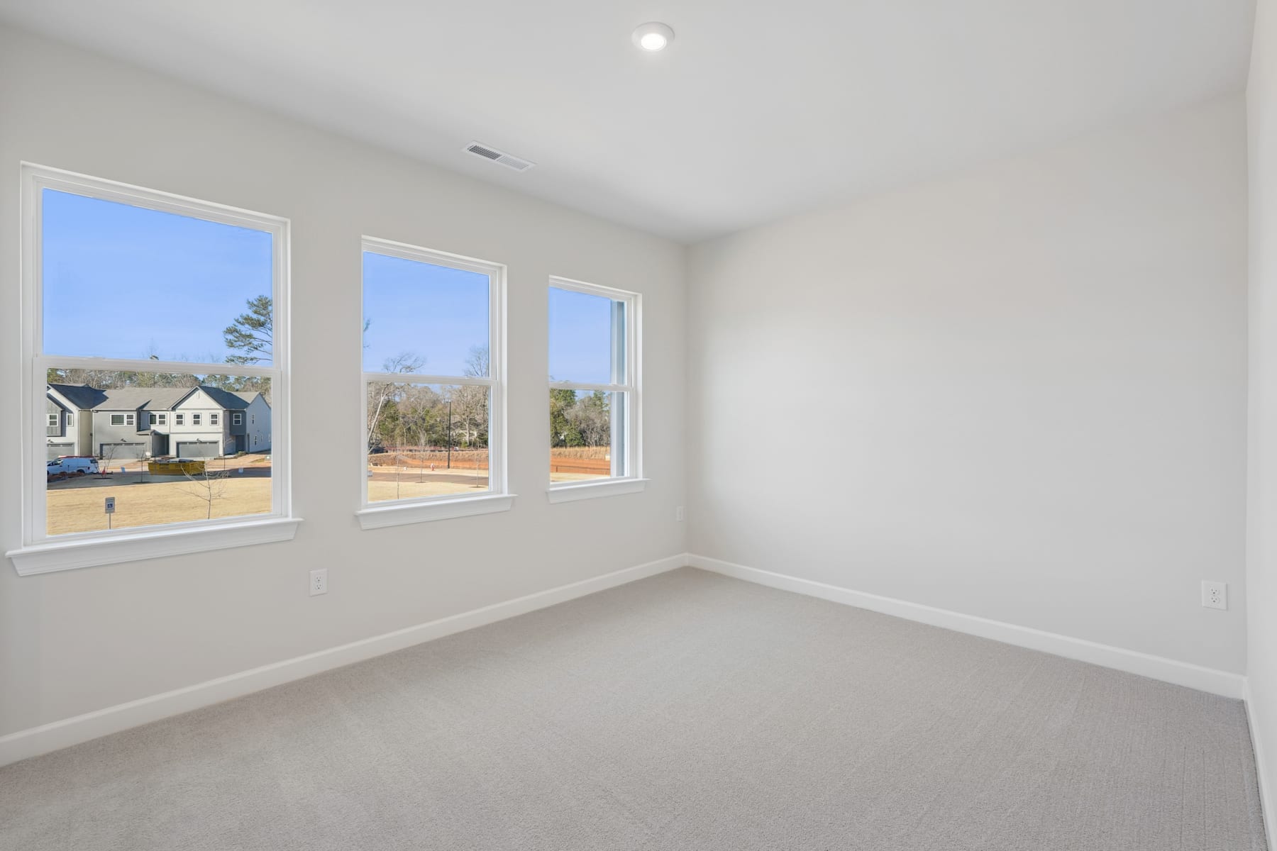 A bright, spacious room with large windows overlooking a residential neighborhood in the background.