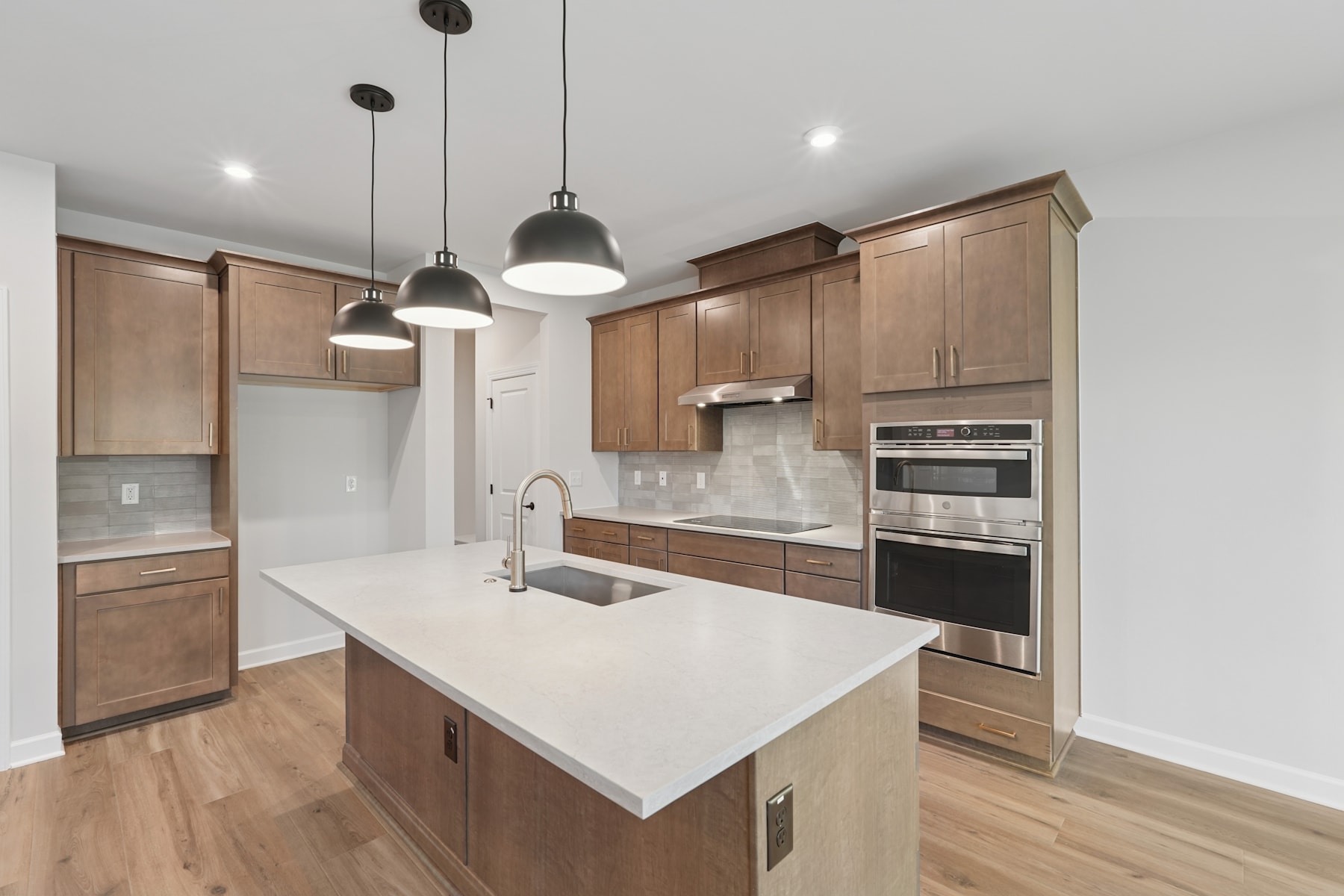 A modern, well-lit kitchen with light wood cabinets, a white countertop, and pendant lights hanging above the island.