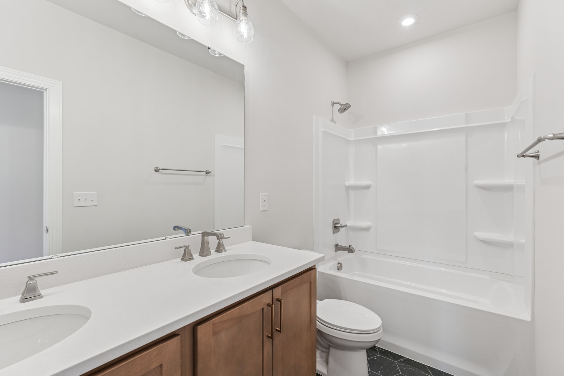 A modern, well-lit bathroom with a double vanity, a toilet, and a bathtub surrounded by white walls and wooden cabinetry.