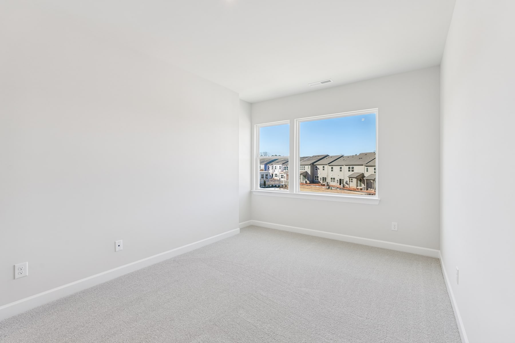 A bright, empty room with a large window overlooking a residential neighborhood in the background.