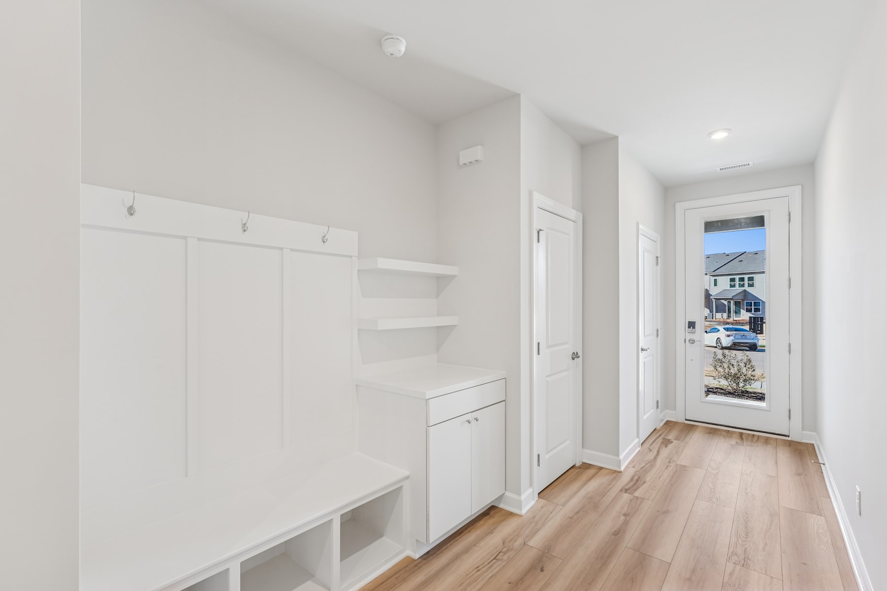 A bright and spacious hallway with white walls, wooden floors, and built-in storage units along the wall.