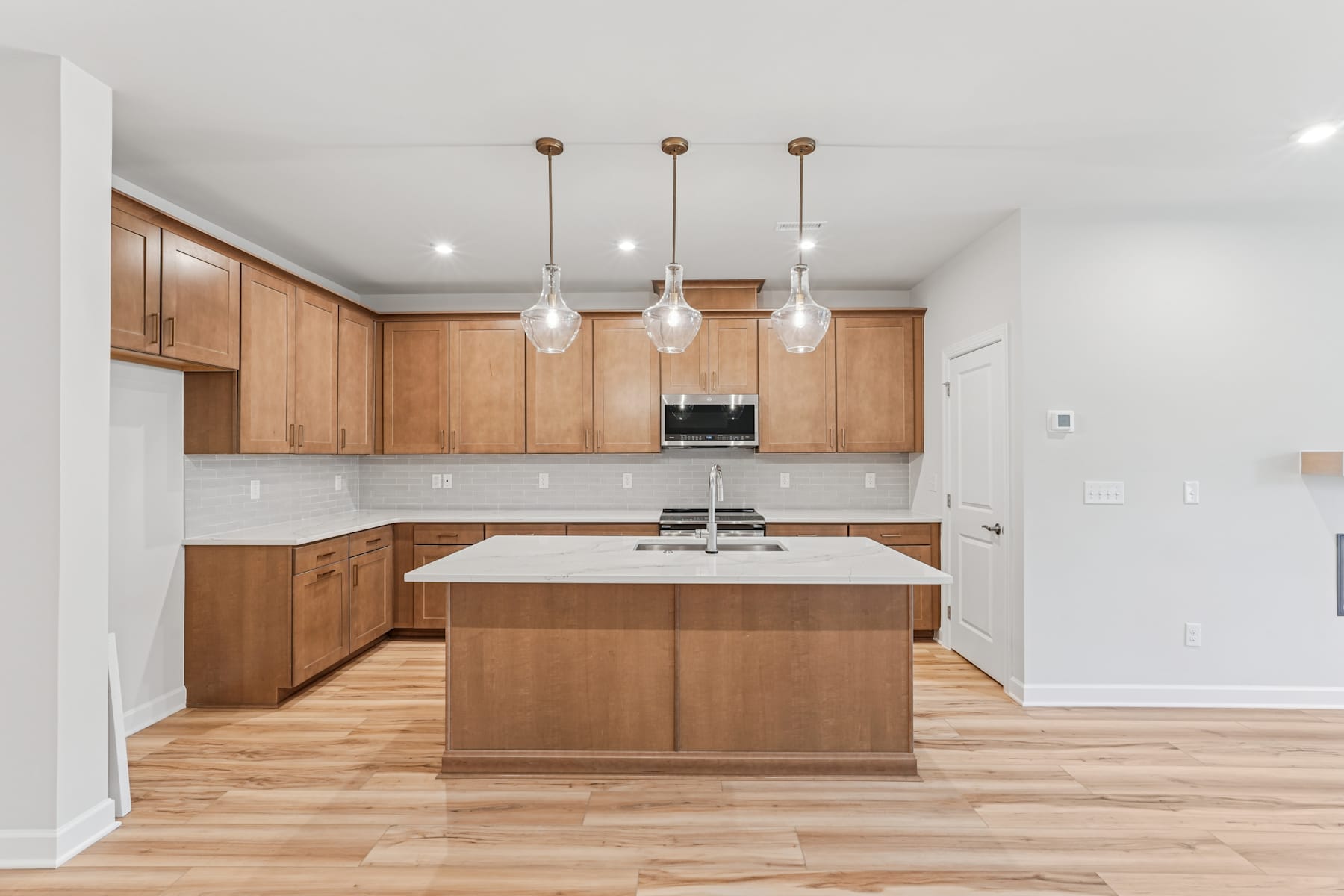 A modern, open-concept kitchen with wooden cabinetry, a central island, and pendant lighting fixtures illuminating the space.