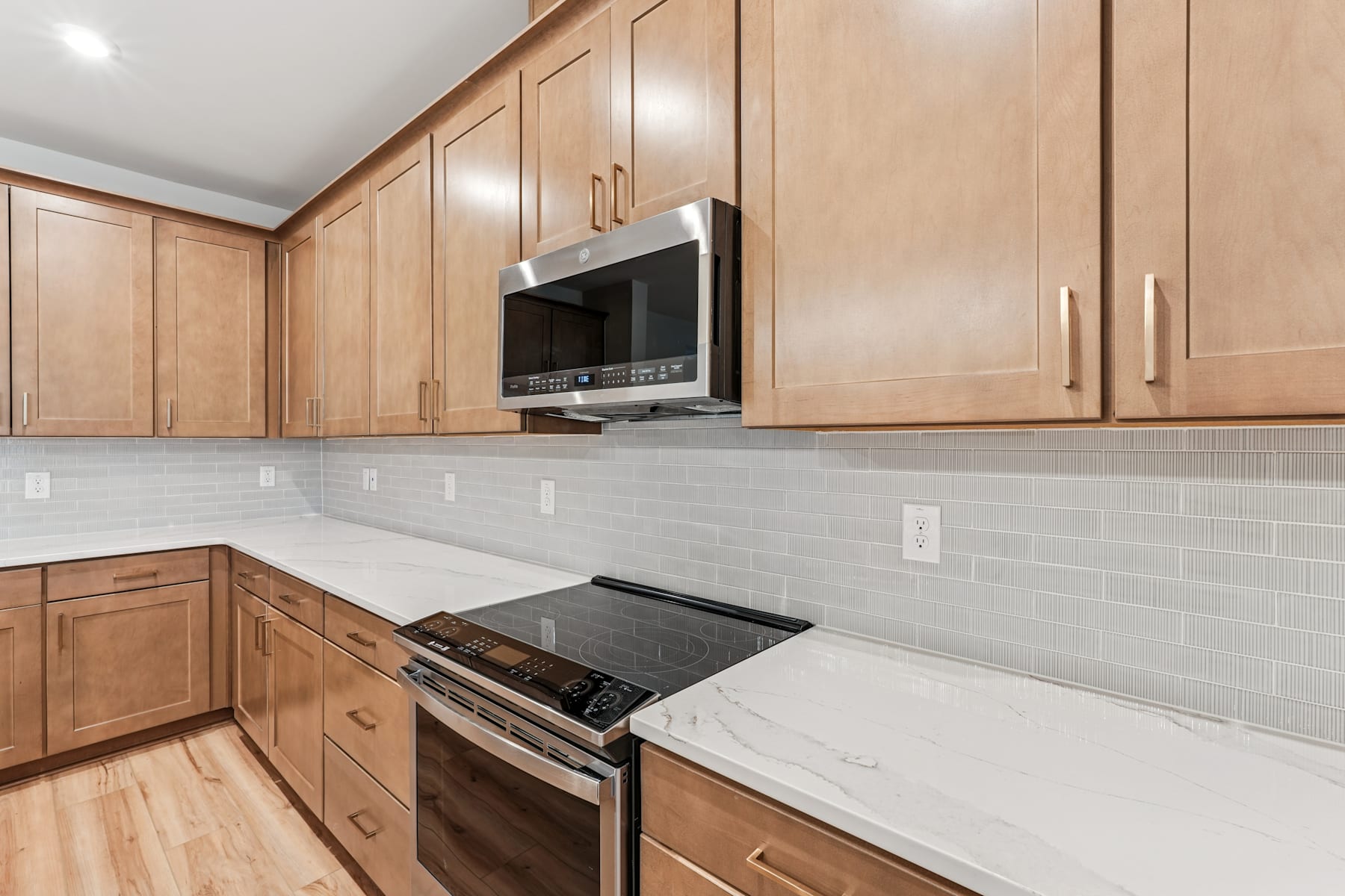 A modern kitchen with light wood cabinets, a white countertop, and a stainless steel oven and microwave.