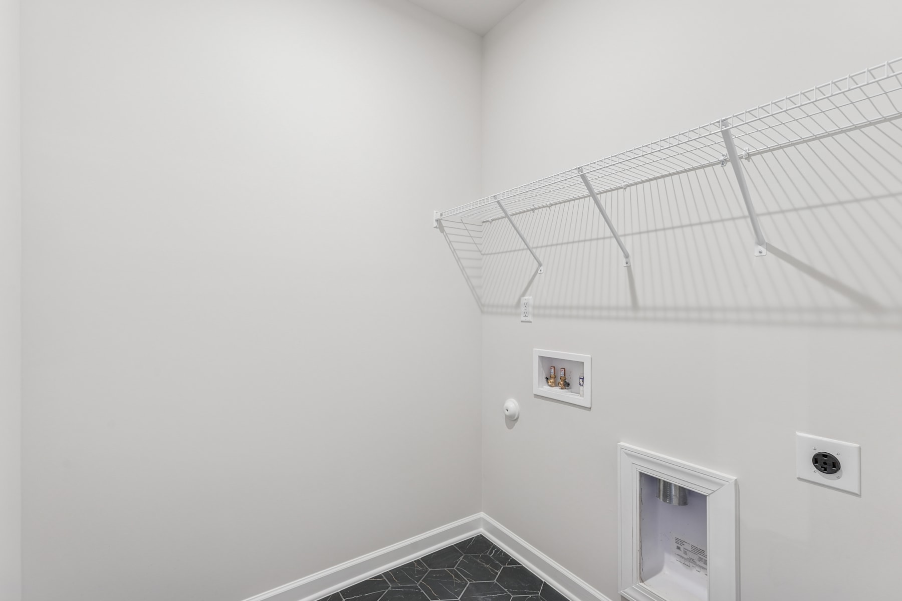 A white, minimalist room with a wire mesh structure mounted on the wall and a small framed artwork hanging nearby.
