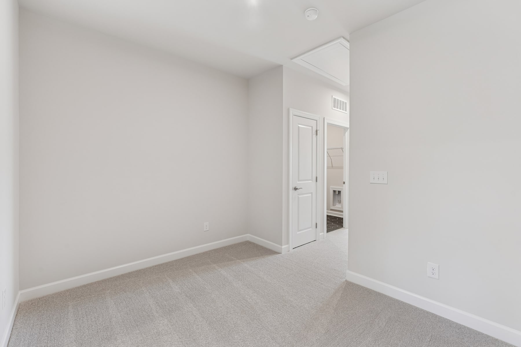 A minimalist, bright, and spacious room with white walls, a wooden floor, and a partially visible doorway leading to another room.