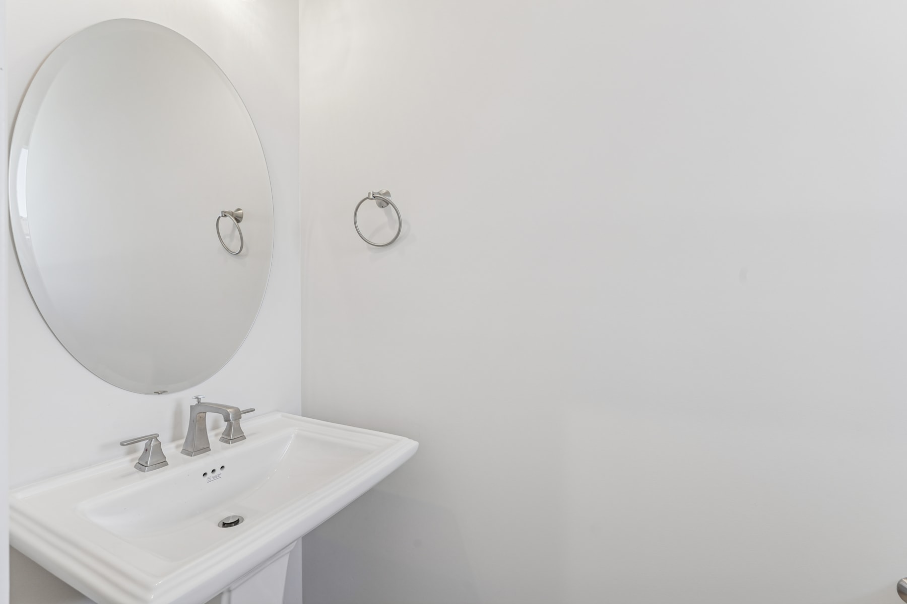 Oval mirrors hang above a white sink in a minimalist bathroom setting with plain white walls.