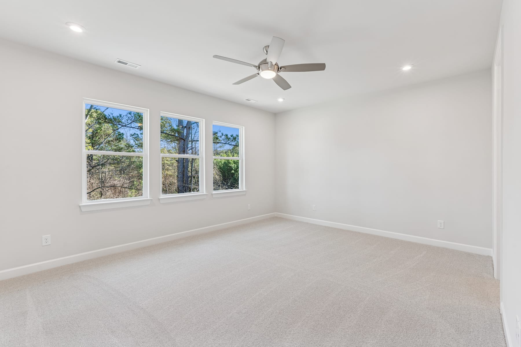 A bright, airy room with large windows overlooking a wooded outdoor scene, featuring a ceiling fan and hardwood flooring.