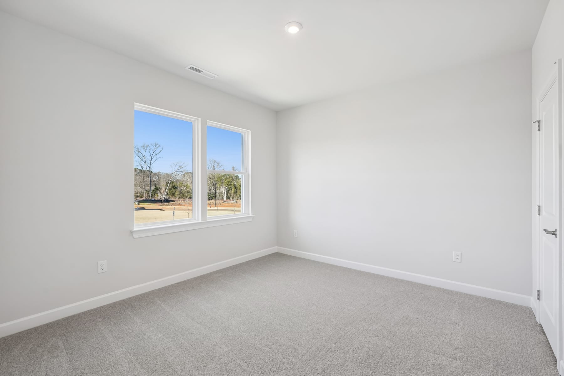 A bright, empty room with large windows overlooking a wooded outdoor area.