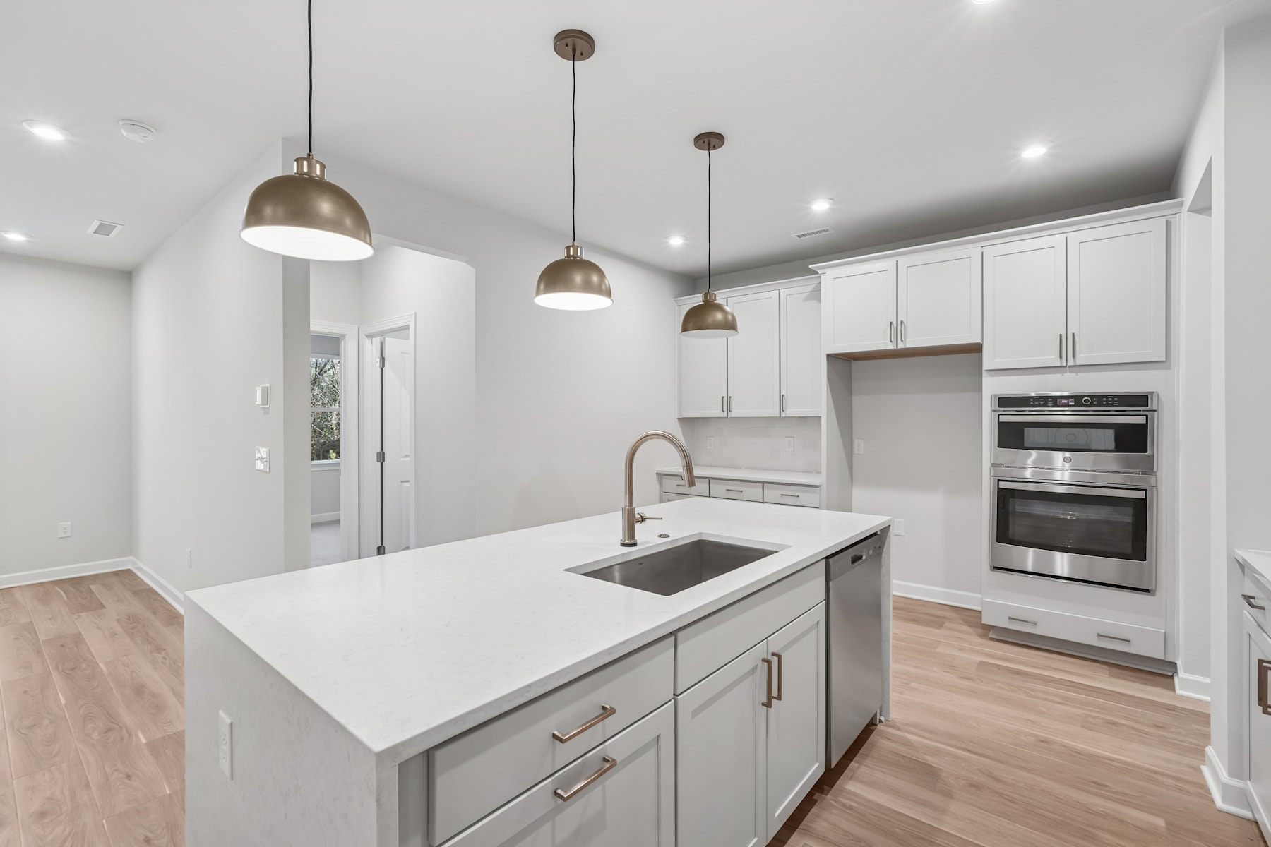 A modern, well-lit kitchen with white cabinets, stainless steel appliances, and a large central island with a sink and countertop.