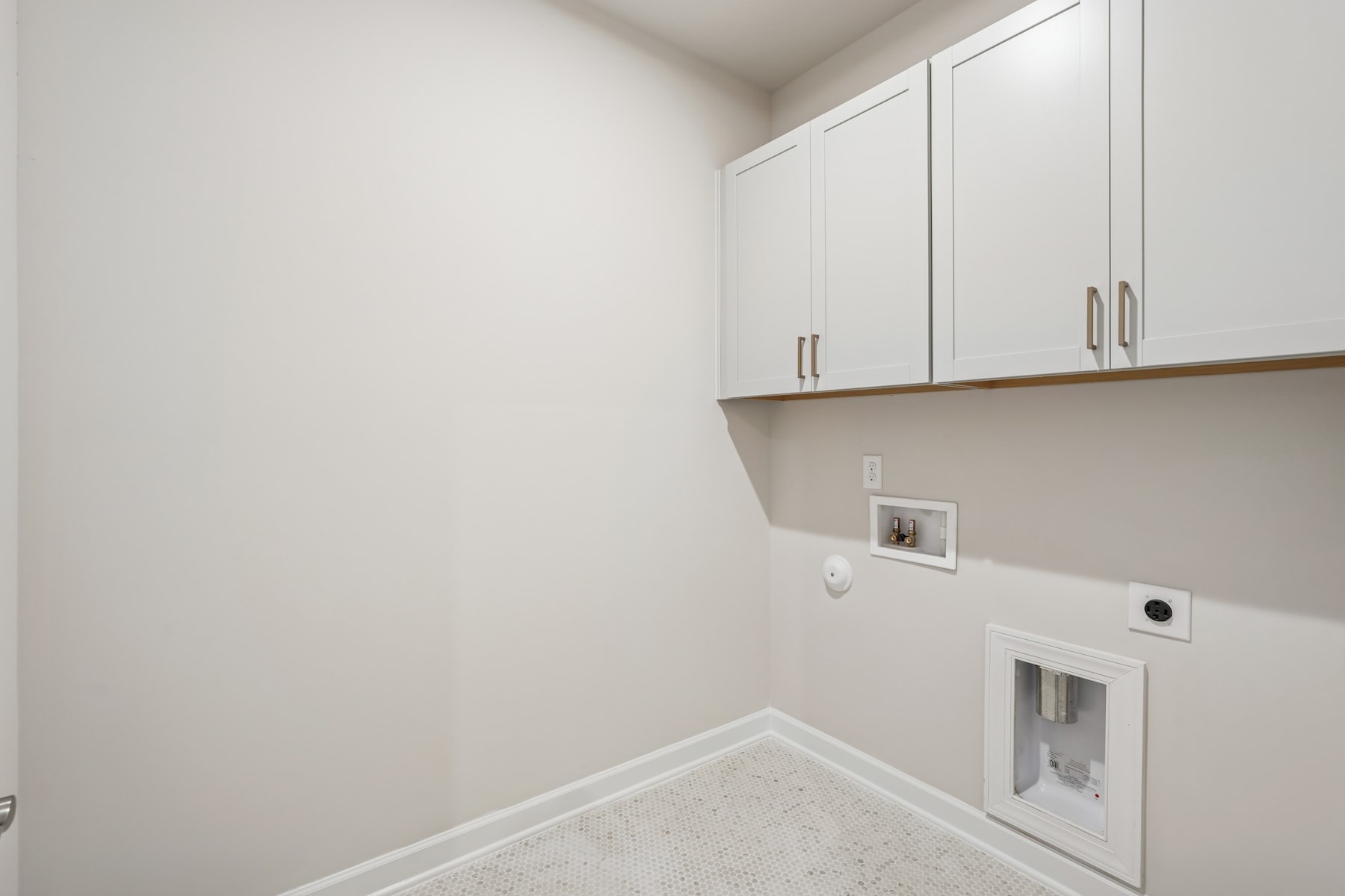 A small, minimalist laundry room with white walls, cabinets, and a washer and dryer unit.