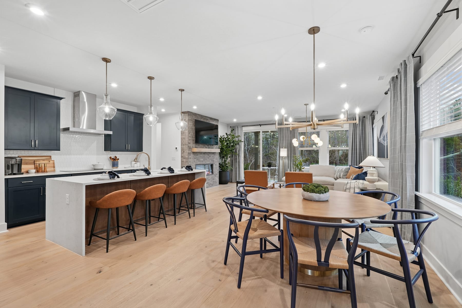 A modern and spacious kitchen and dining area with a large wooden table, comfortable chairs, and a sleek kitchen with dark cabinets and stainless steel appliances.