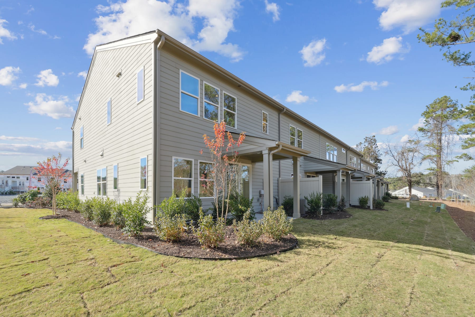A modern two-story townhouse with a well-manicured lawn and landscaping in the foreground, set against a backdrop of a blue sky with fluffy white clouds.