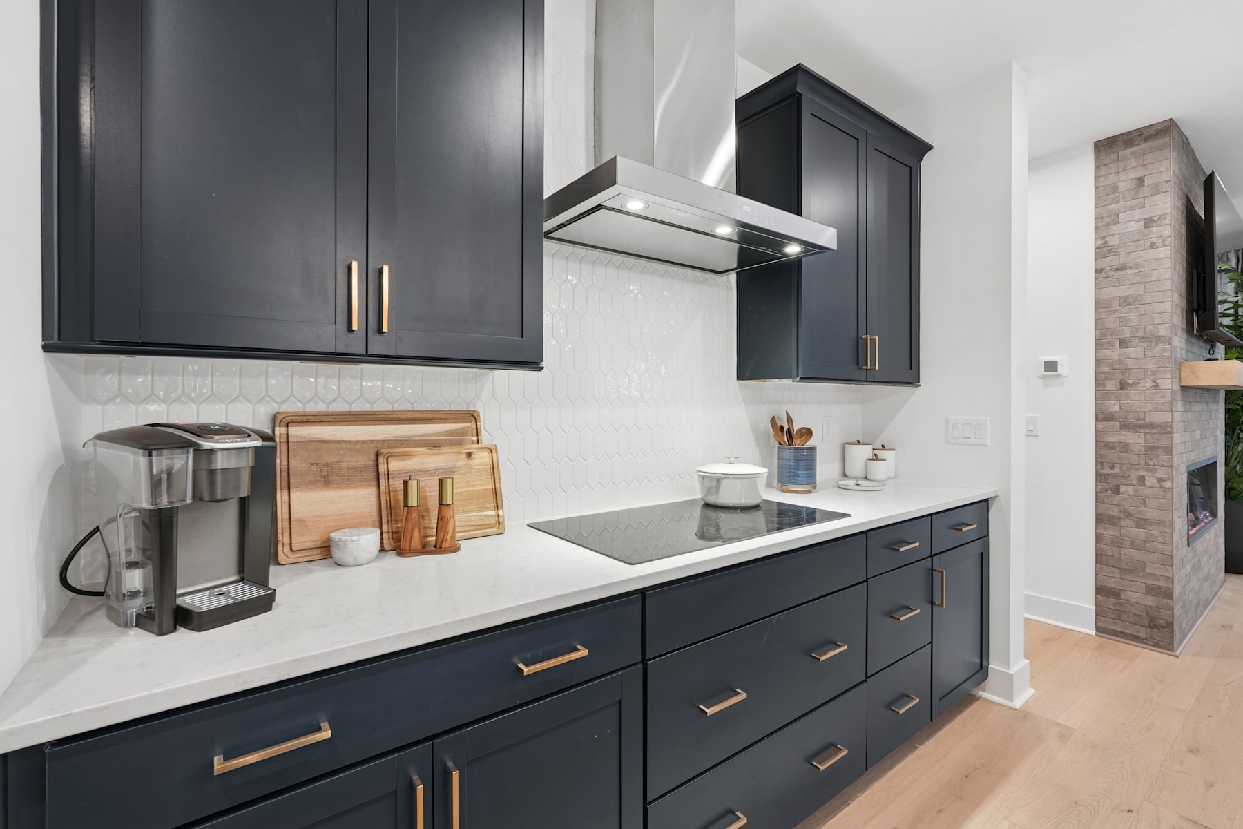 A modern, minimalist kitchen with dark gray cabinets, a white countertop, and various kitchen accessories and appliances on the counter.