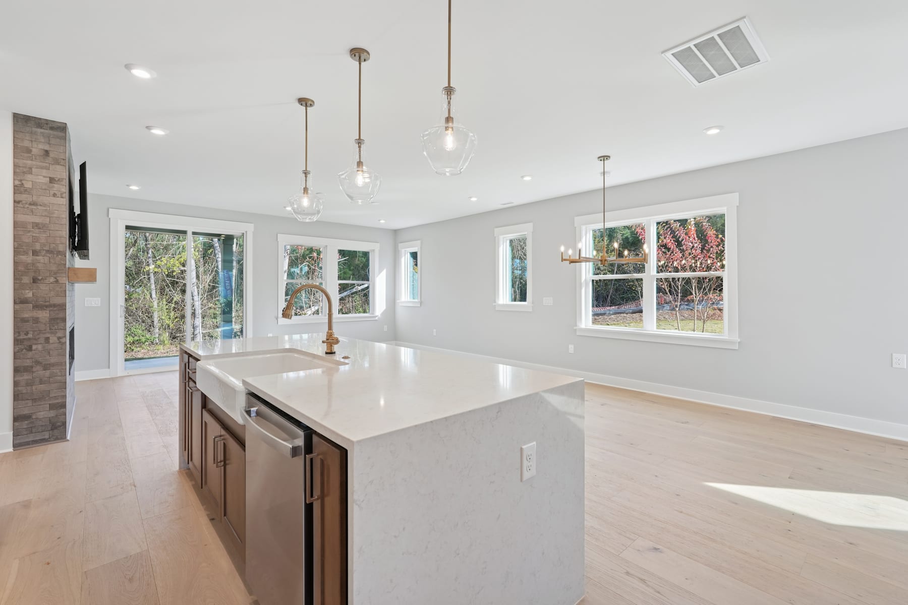 A modern, open-concept kitchen with a large island, pendant lighting, and large windows overlooking a wooded outdoor area.