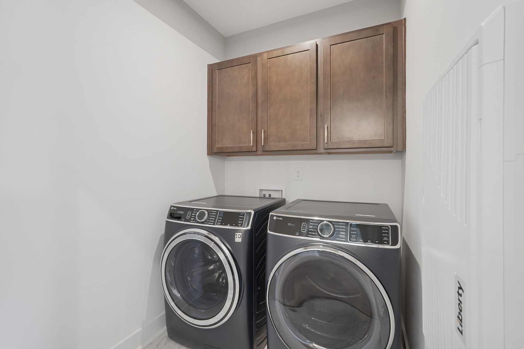 The image shows a laundry room with wooden cabinets above a washer and dryer, both of which are modern and black in color.